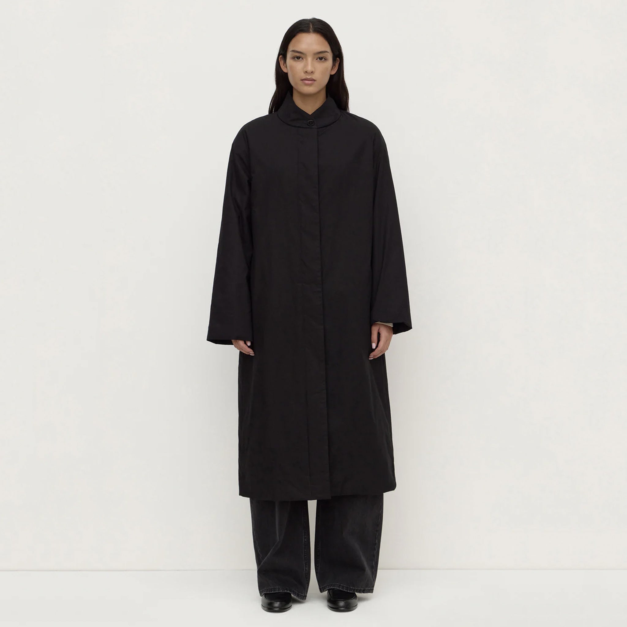 Model wearing the Assembly Label Zoie Padded Coat - Black, a long, sleek design with a collarless silhouette.