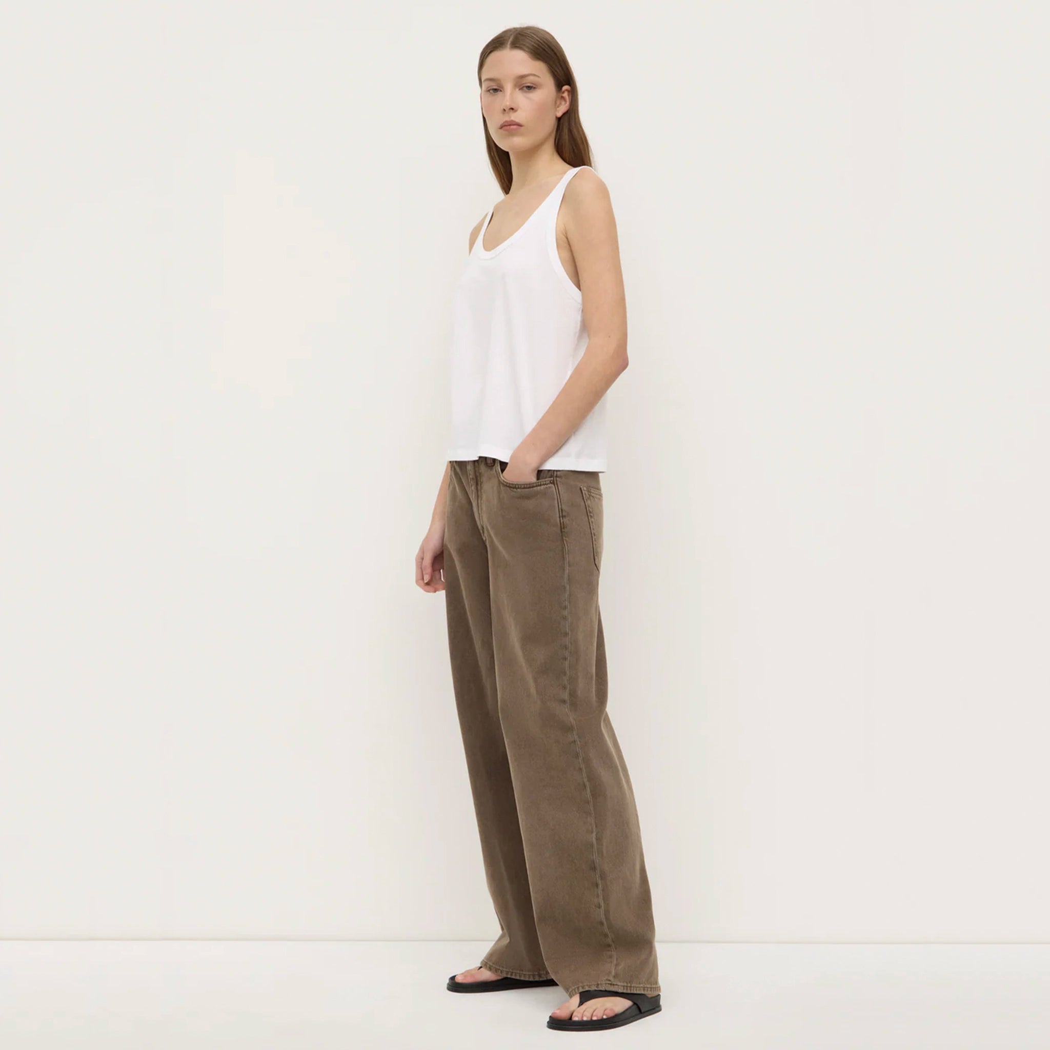 Woman wearing a white sleeveless top and brown pants against a white background