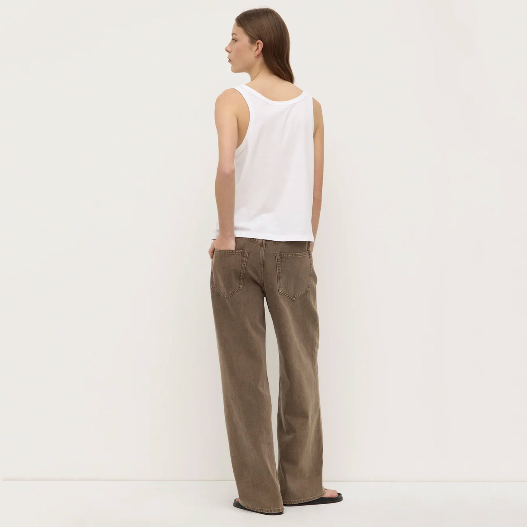 Woman wearing a white sleeveless top and brown pants on a white background