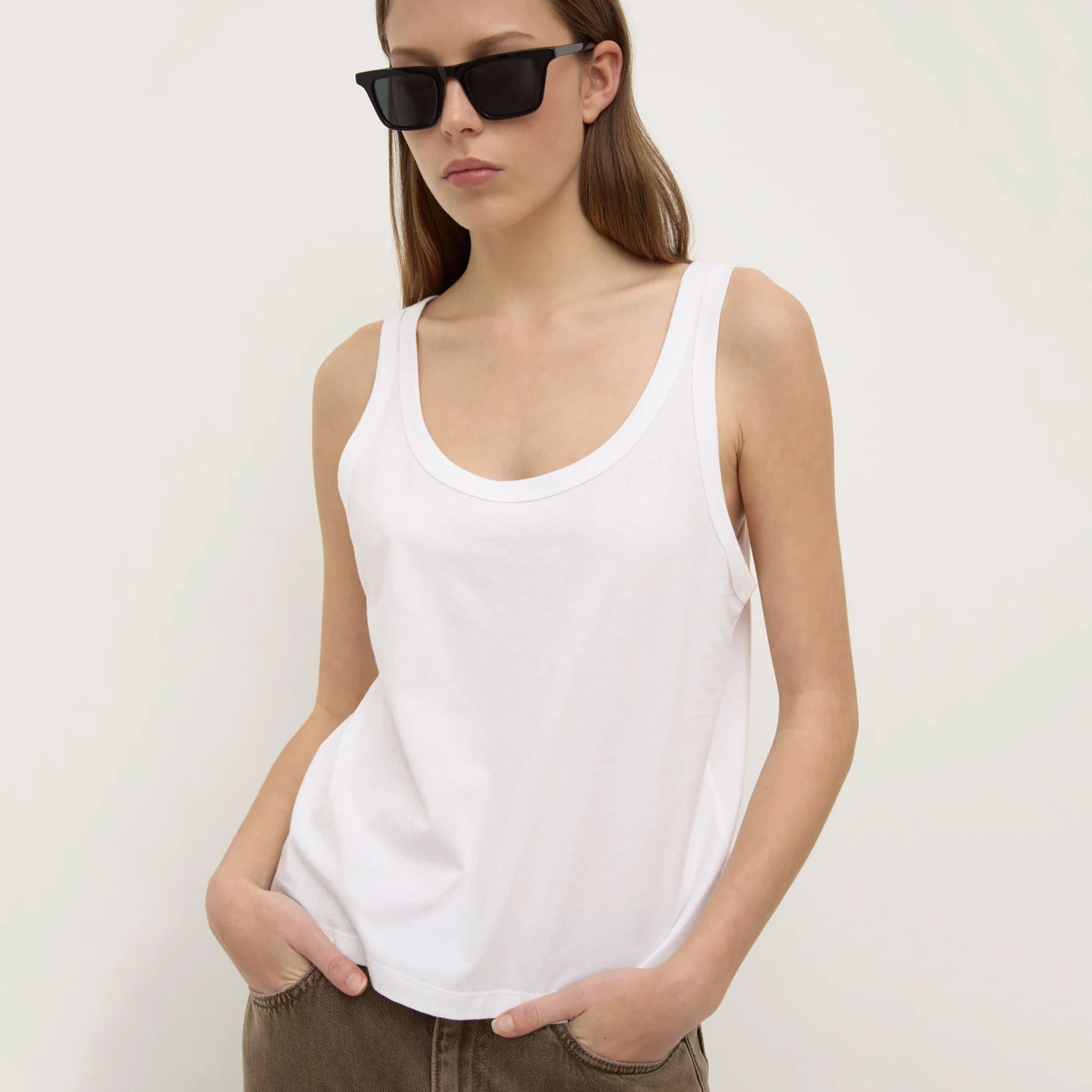 Woman wearing a white tank top and sunglasses against a plain background