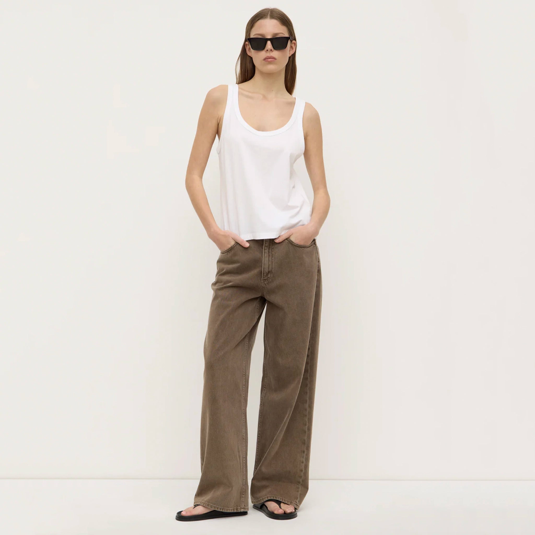 Woman wearing a white tank top and brown wide-leg pants on a white background