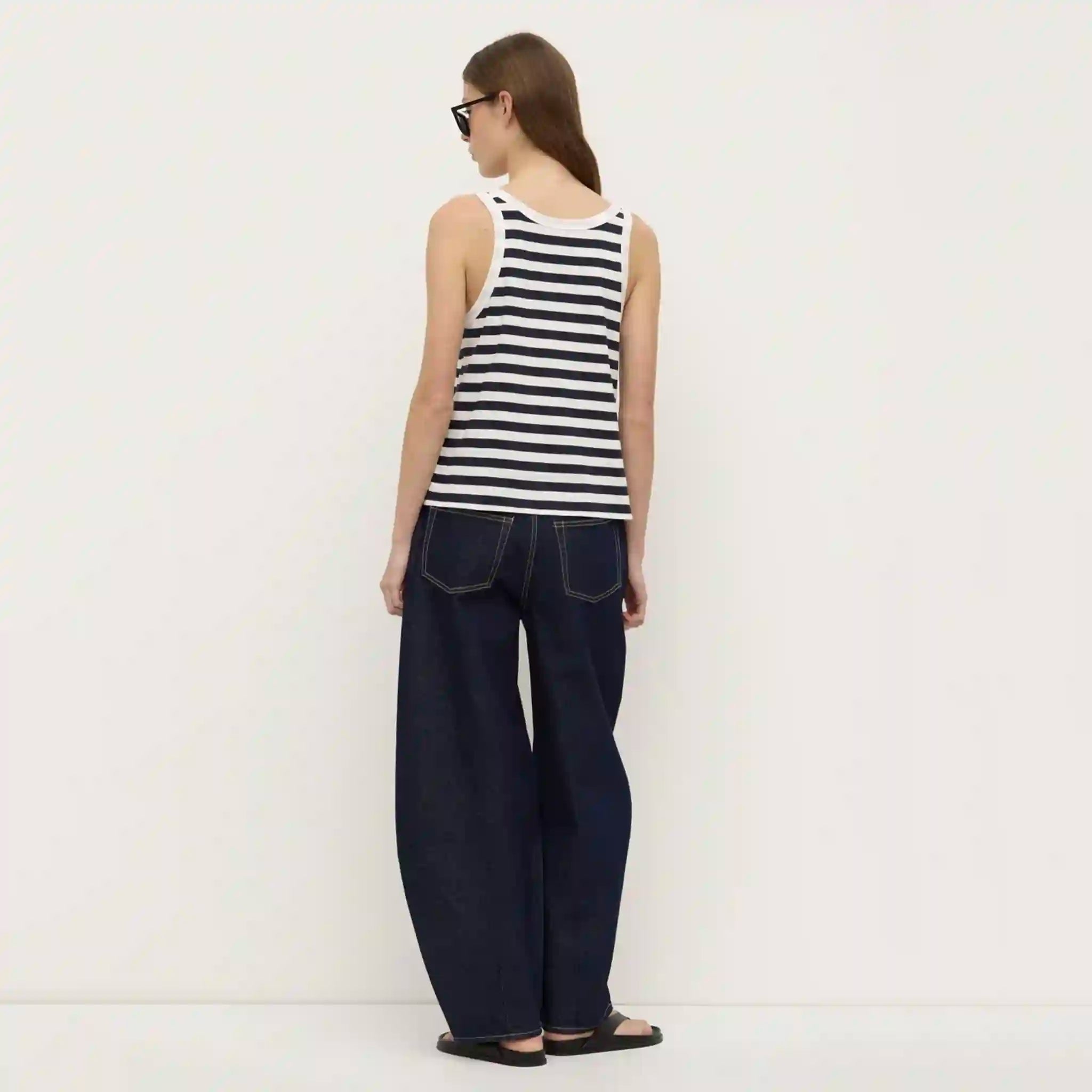 Person wearing a black and white striped sleeveless top and dark blue jeans on a white background