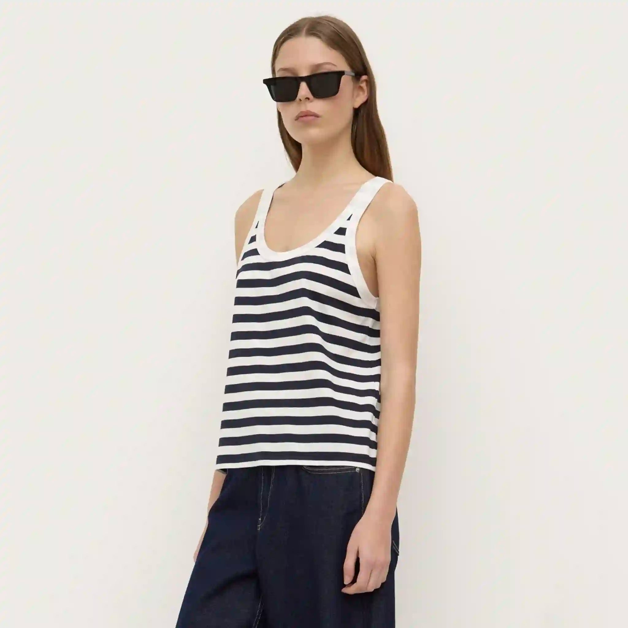 Woman wearing a black and white striped tank top and sunglasses on a plain background