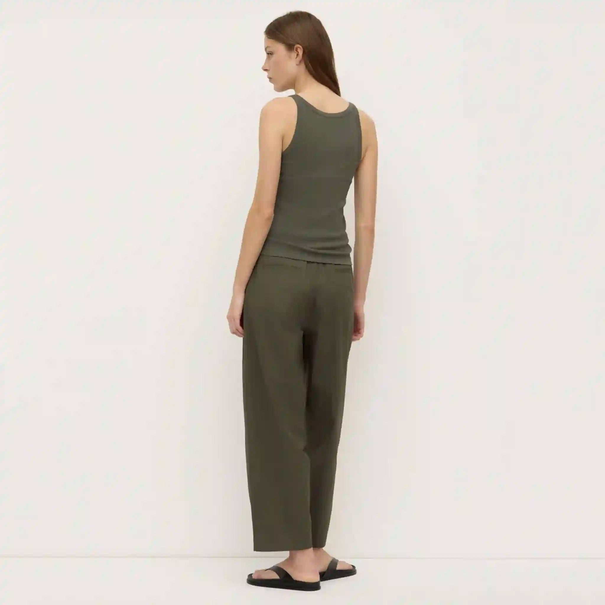 Woman wearing a green sleeveless top and pants against a white background