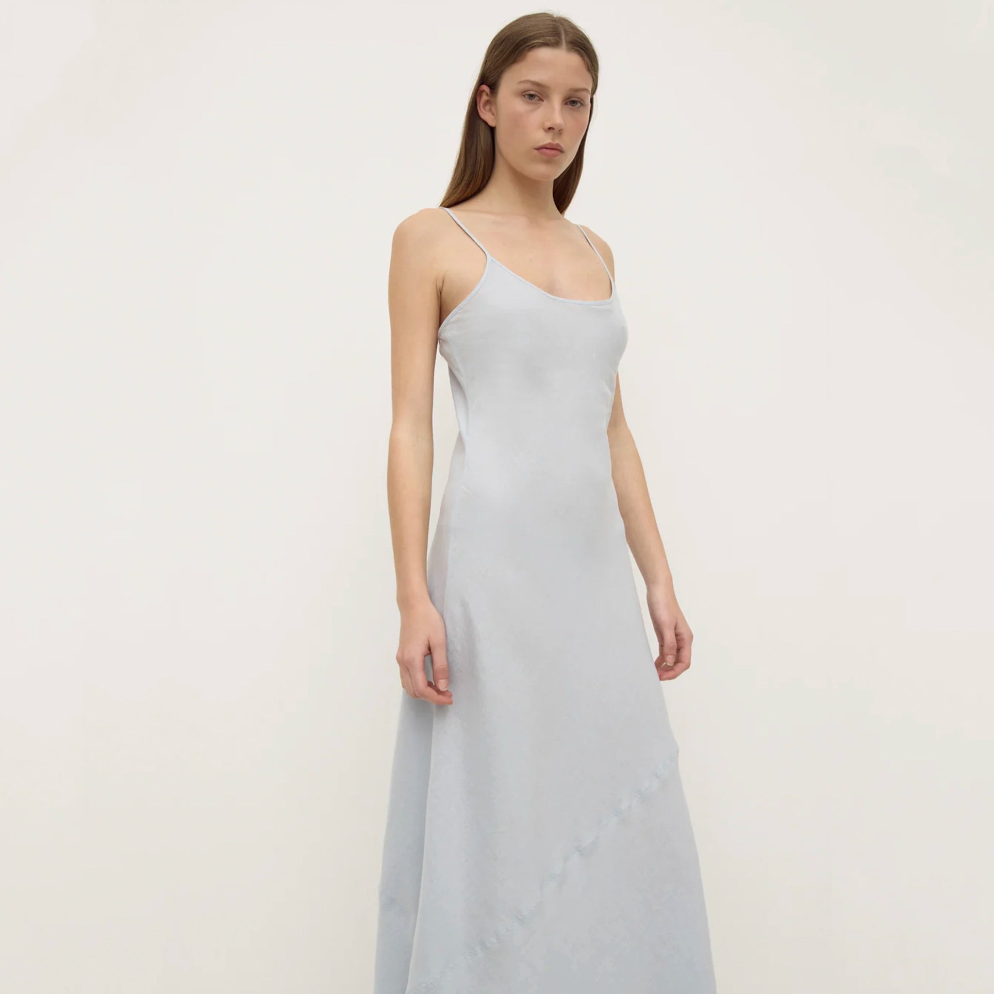 Woman wearing a light gray slip dress against a plain background