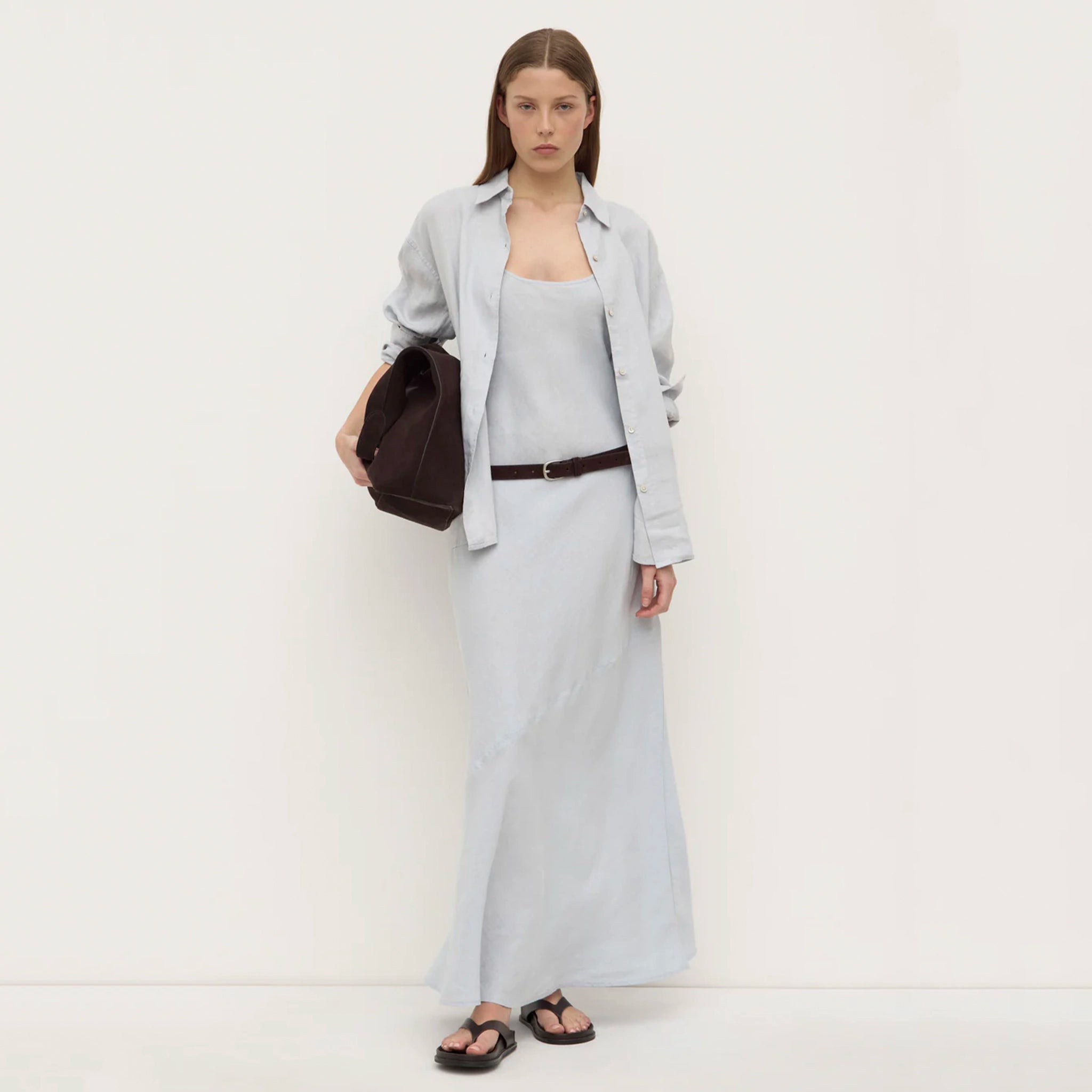 Woman wearing a light gray outfit with a brown bag on a white background