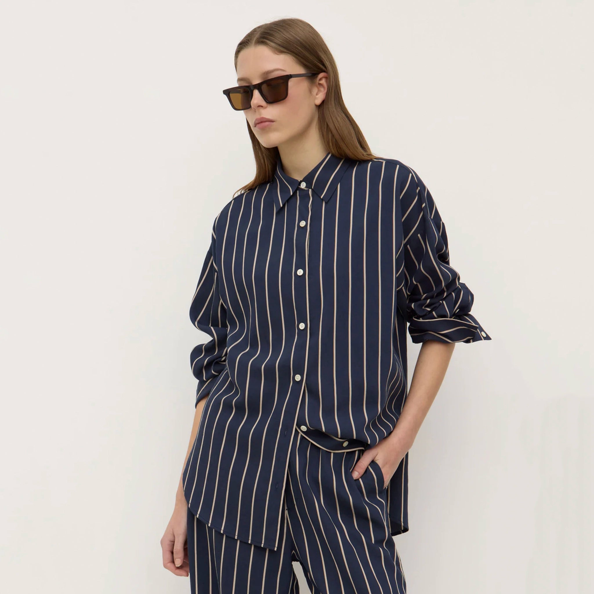 Person wearing a navy striped shirt and pants with sunglasses on a white background