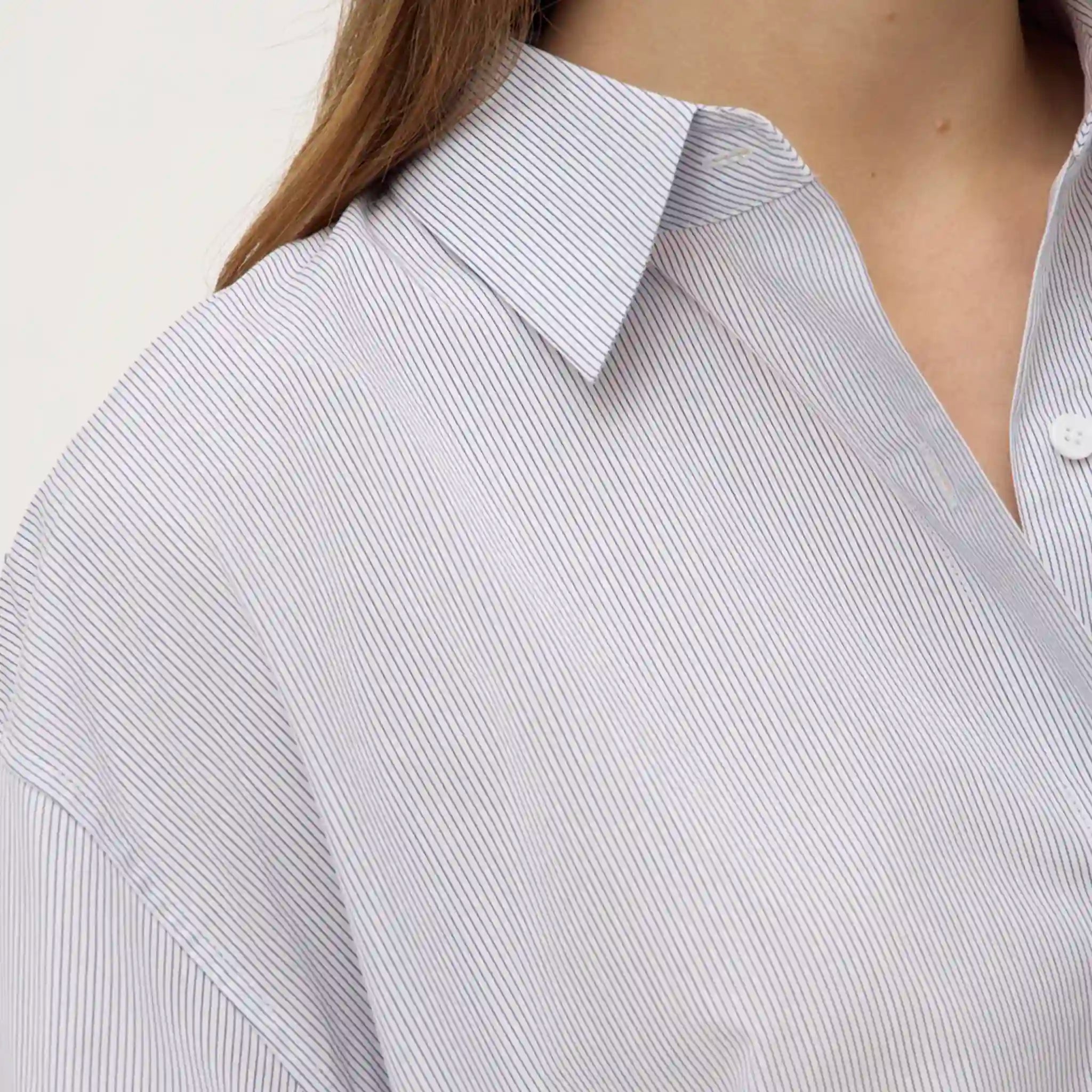 Close-up of a person wearing a light blue and white striped shirt with a plain background