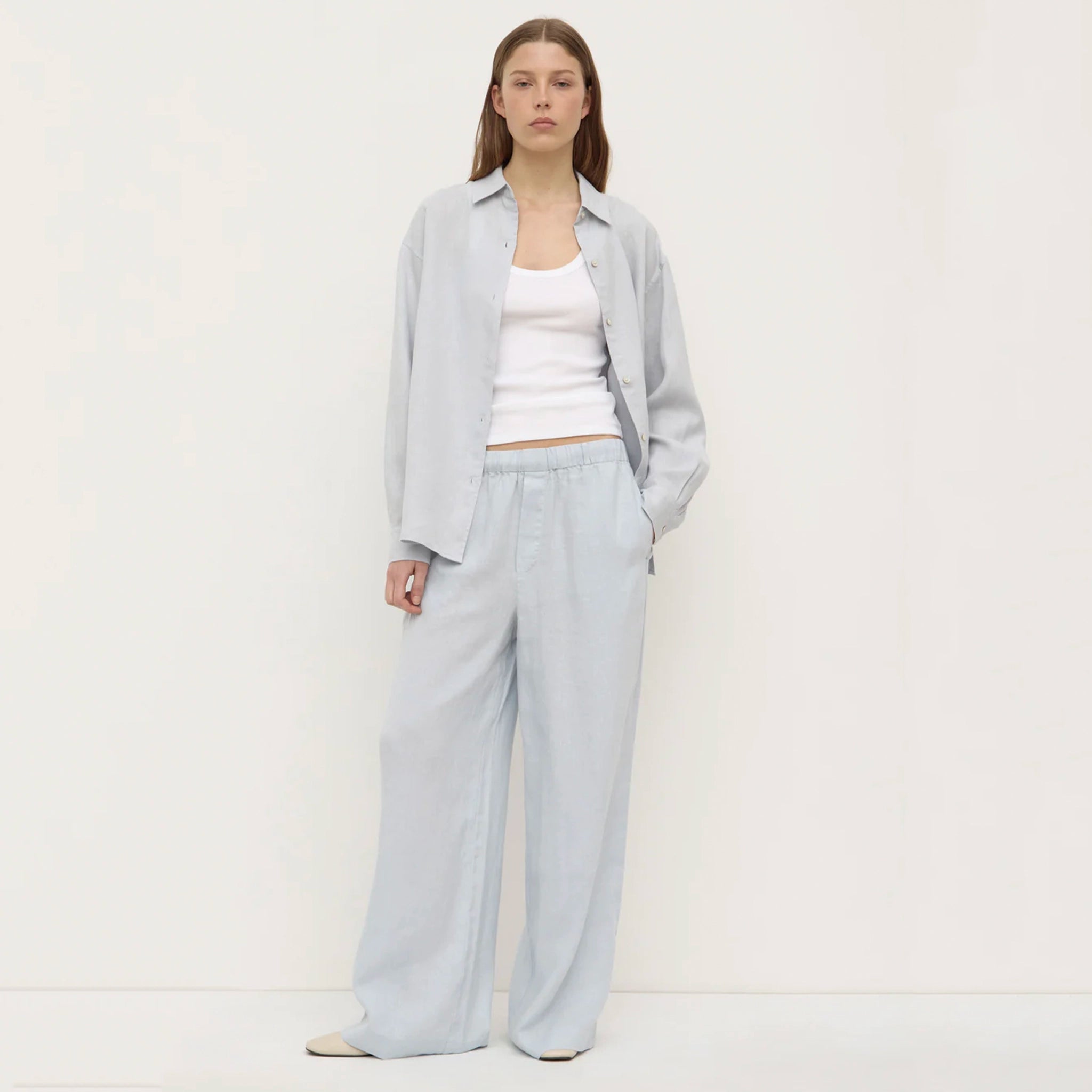 Woman wearing a light gray outfit with a white top on a plain background