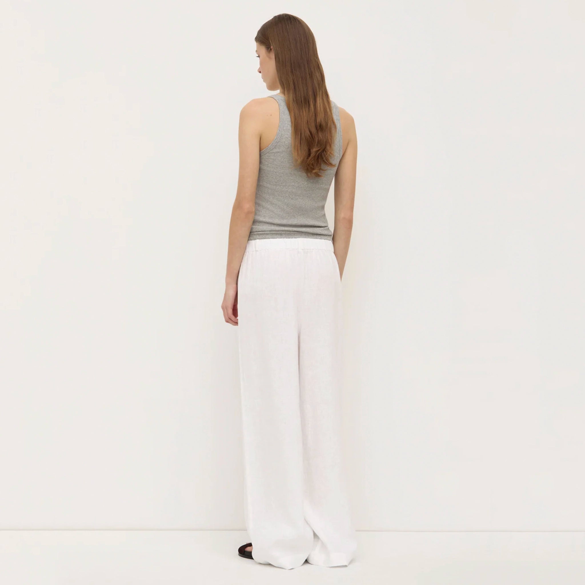 Woman wearing a gray tank top and white pants on a plain background