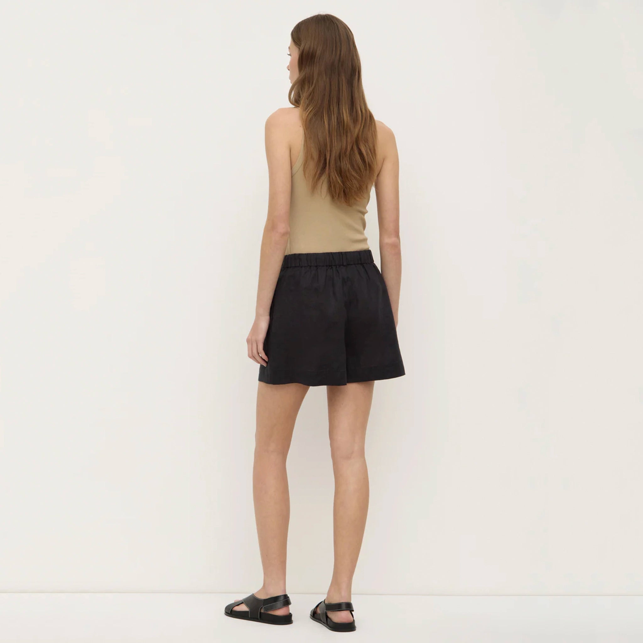 Woman wearing black shorts and a beige top on a white background