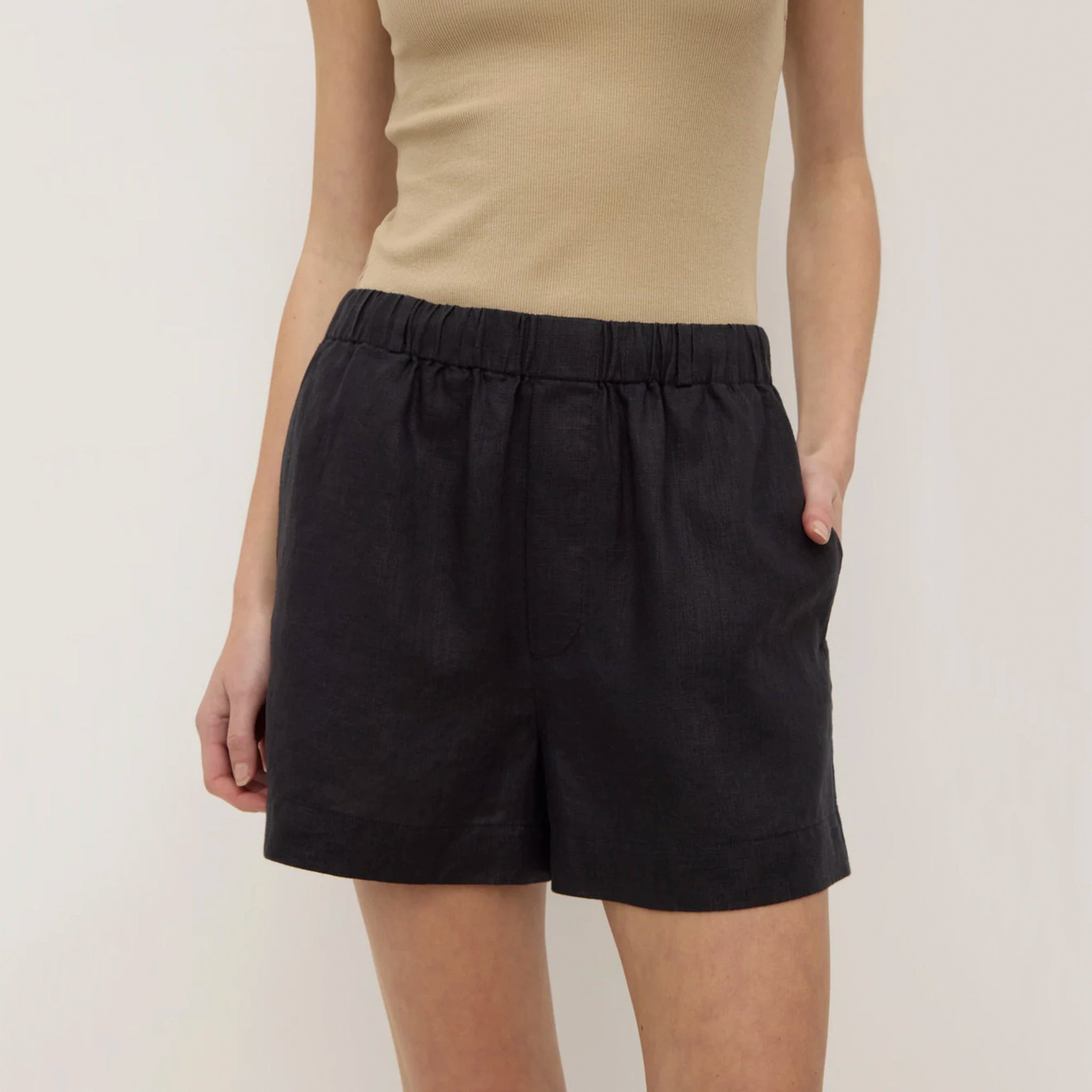 Person wearing black shorts and a beige top on a plain background