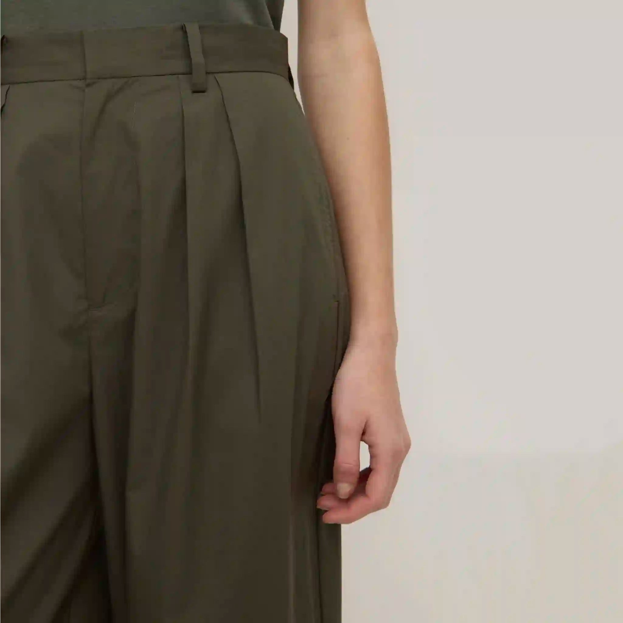 Person wearing olive green pleated pants on a plain background