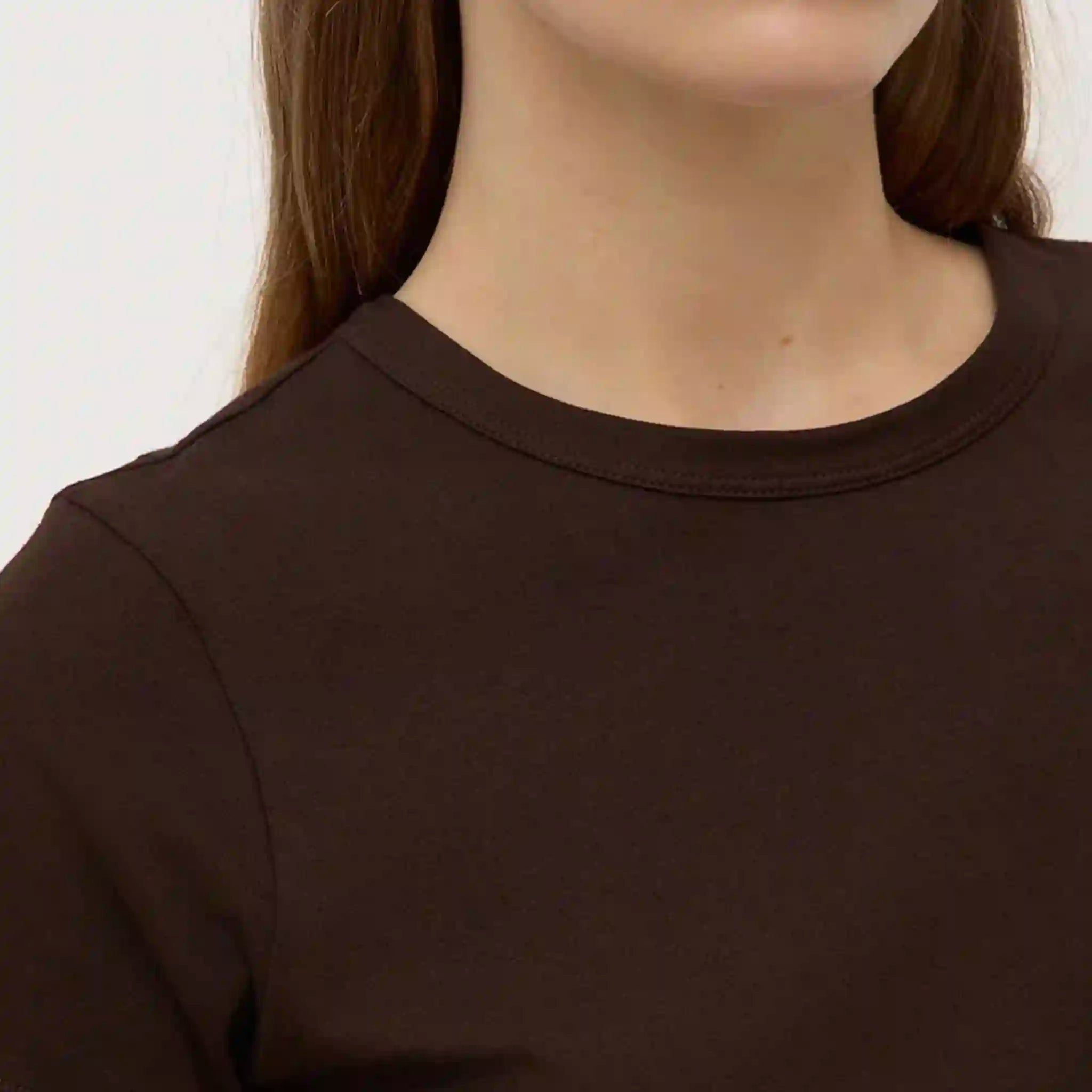 Close-up of a person wearing a plain brown t-shirt against a neutral background