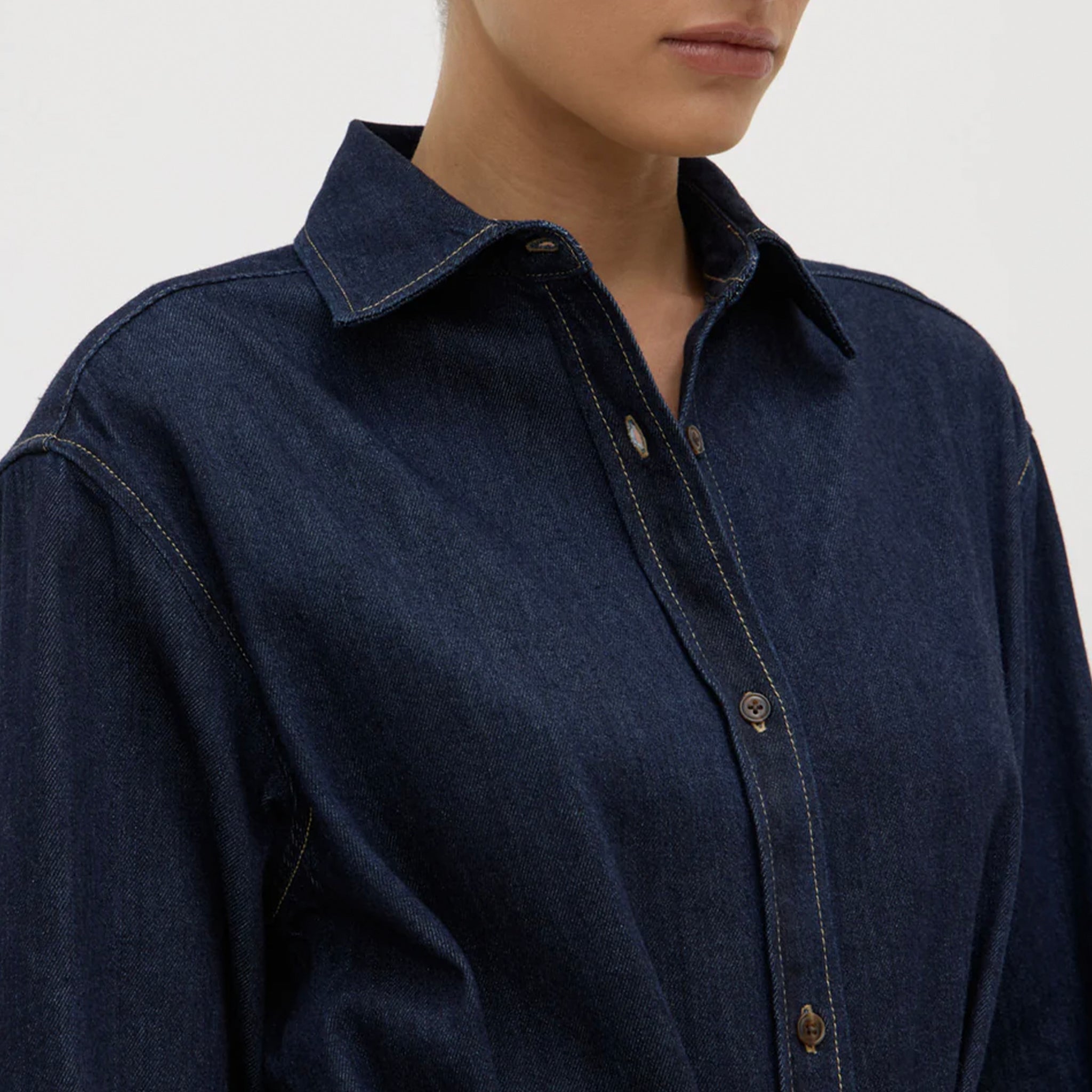 Navy blue denim shirt worn by a person on a light gray background