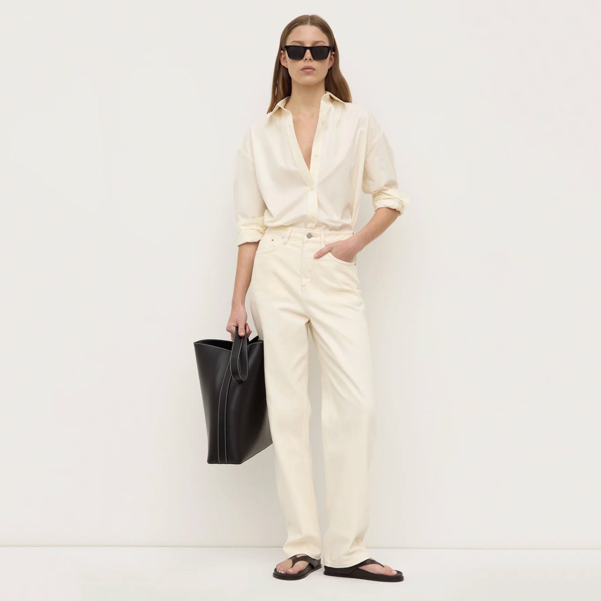 Woman in a white outfit holding a black bag against a white background