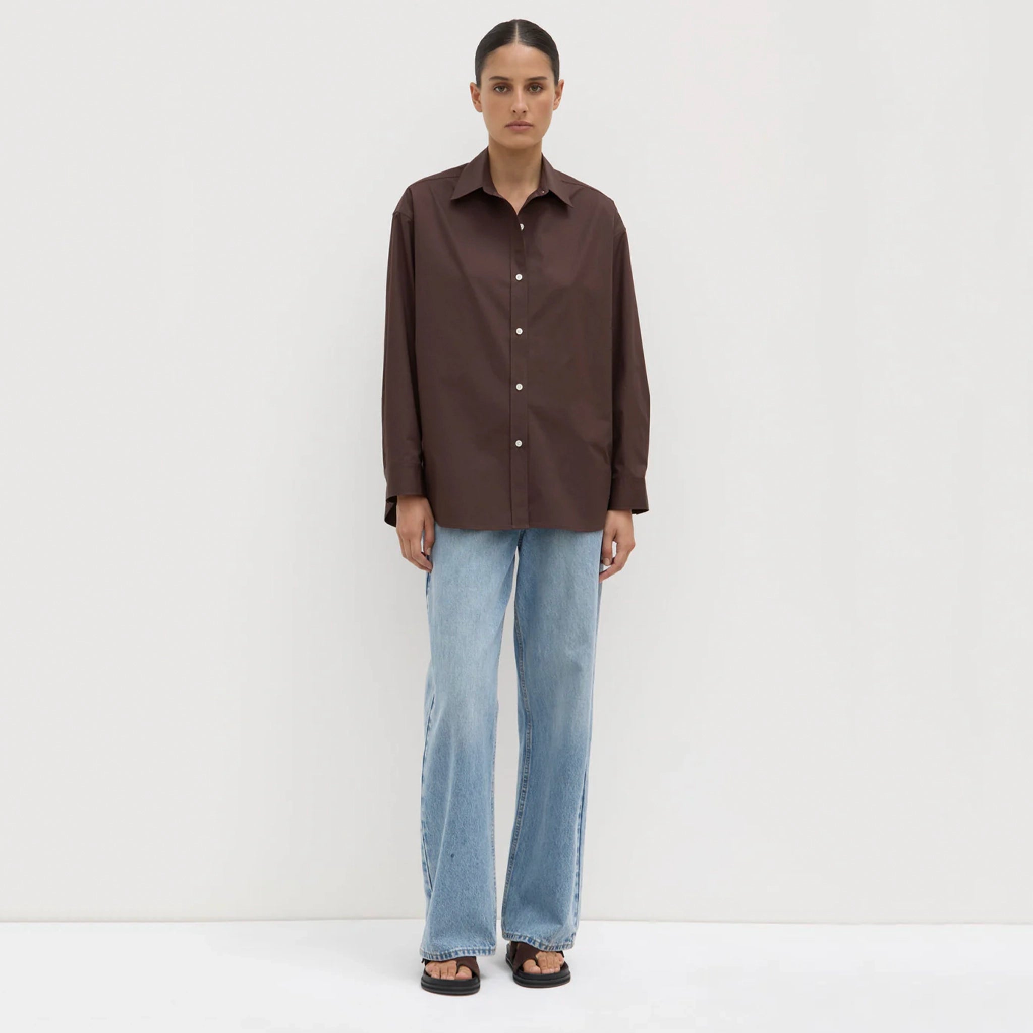 Person wearing a brown shirt and light blue jeans against a white background