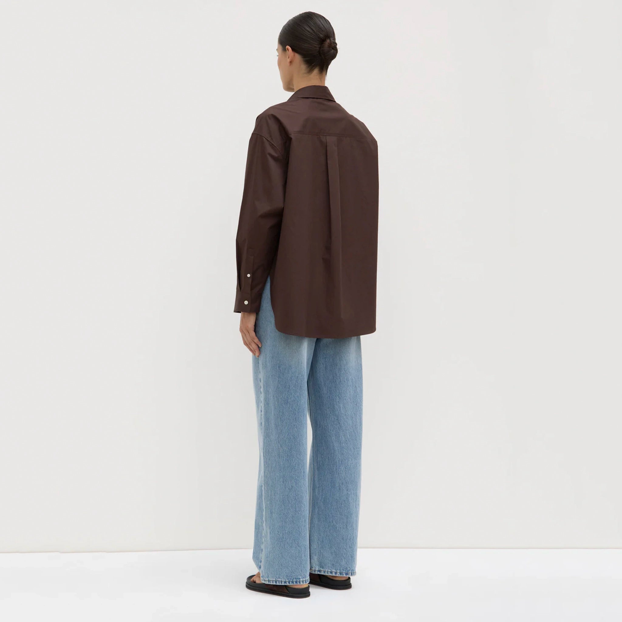 Person wearing a brown jacket and blue jeans on a white background