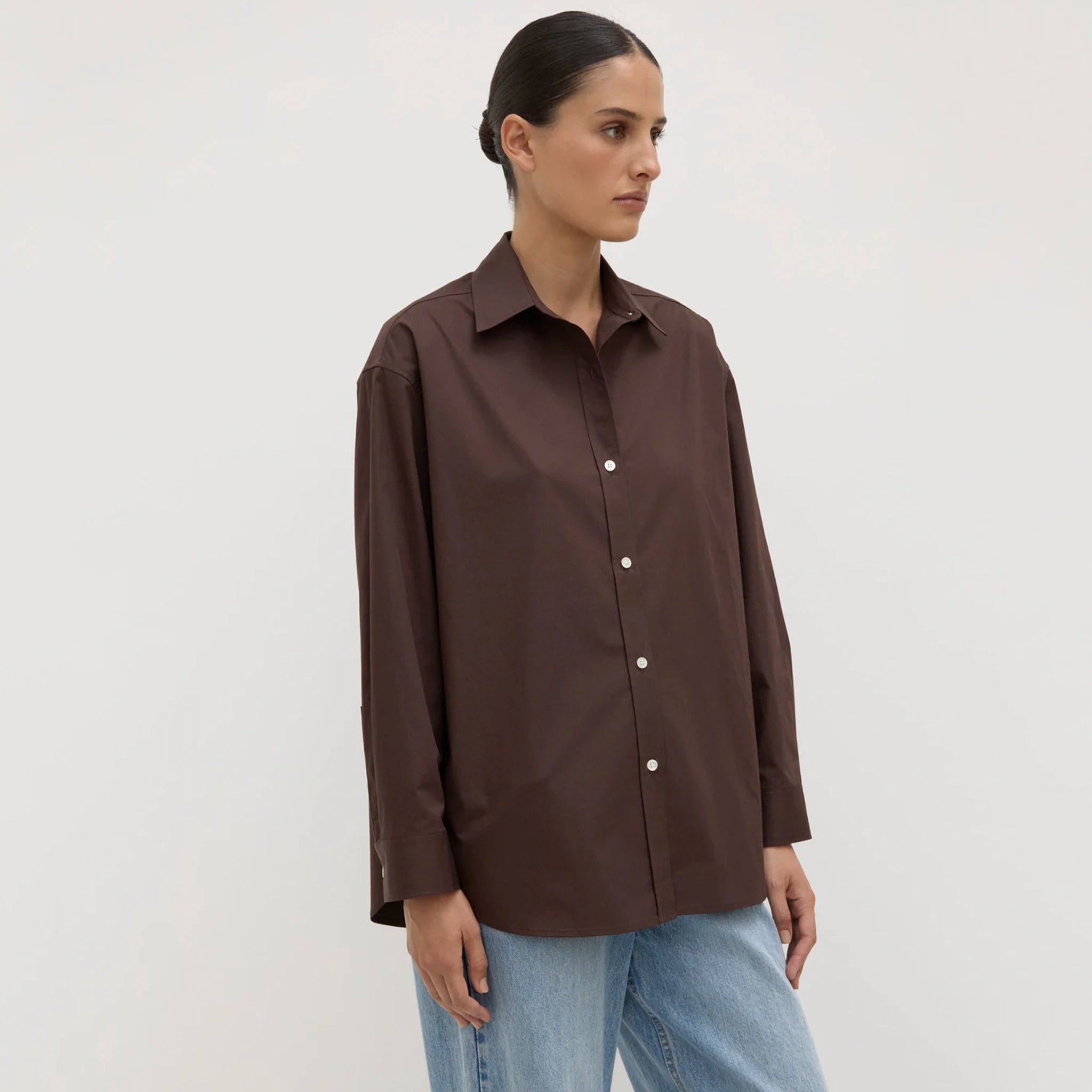 Woman wearing a brown shirt and blue jeans against a white background
