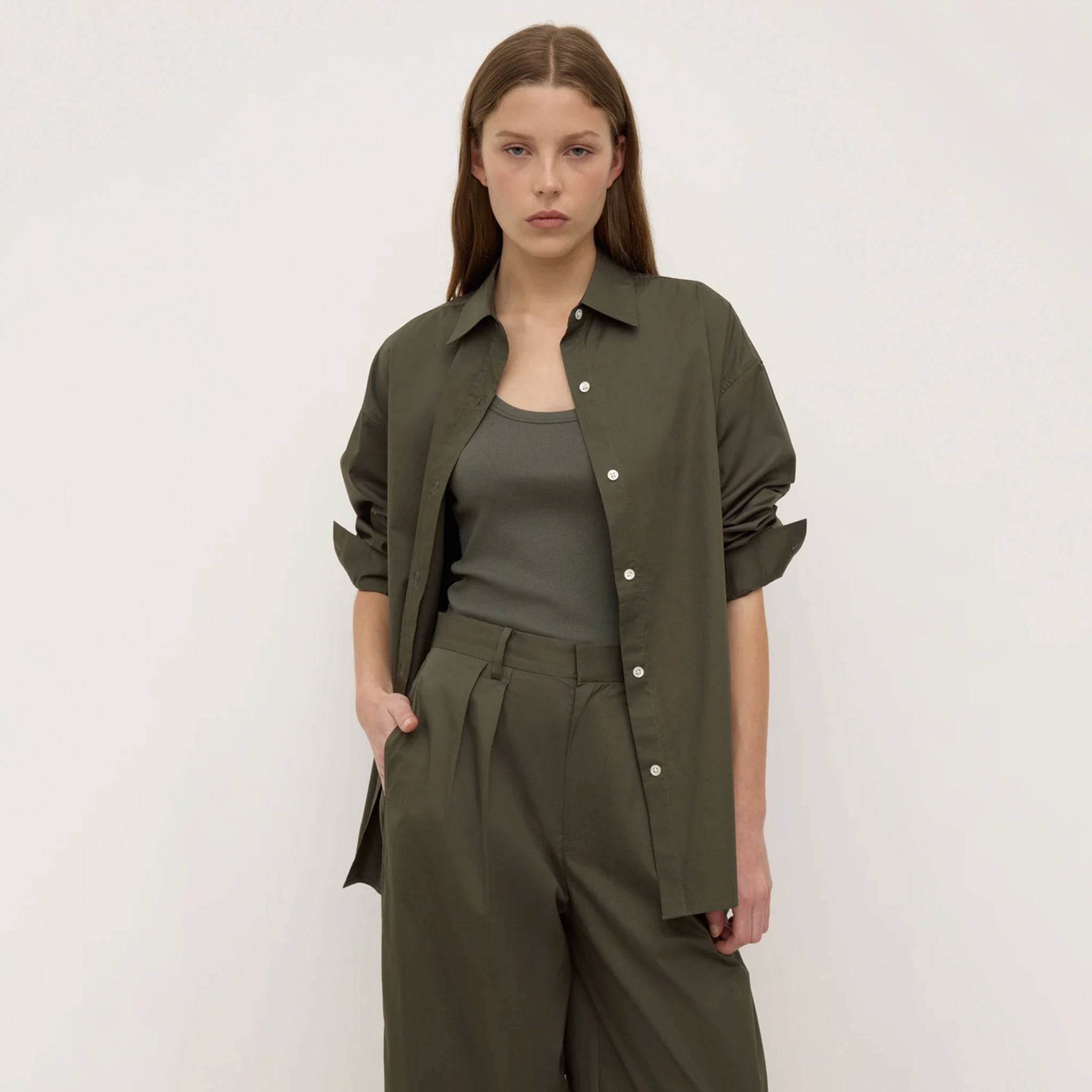 Woman wearing an olive green outfit with a shirt and pants on a white background
