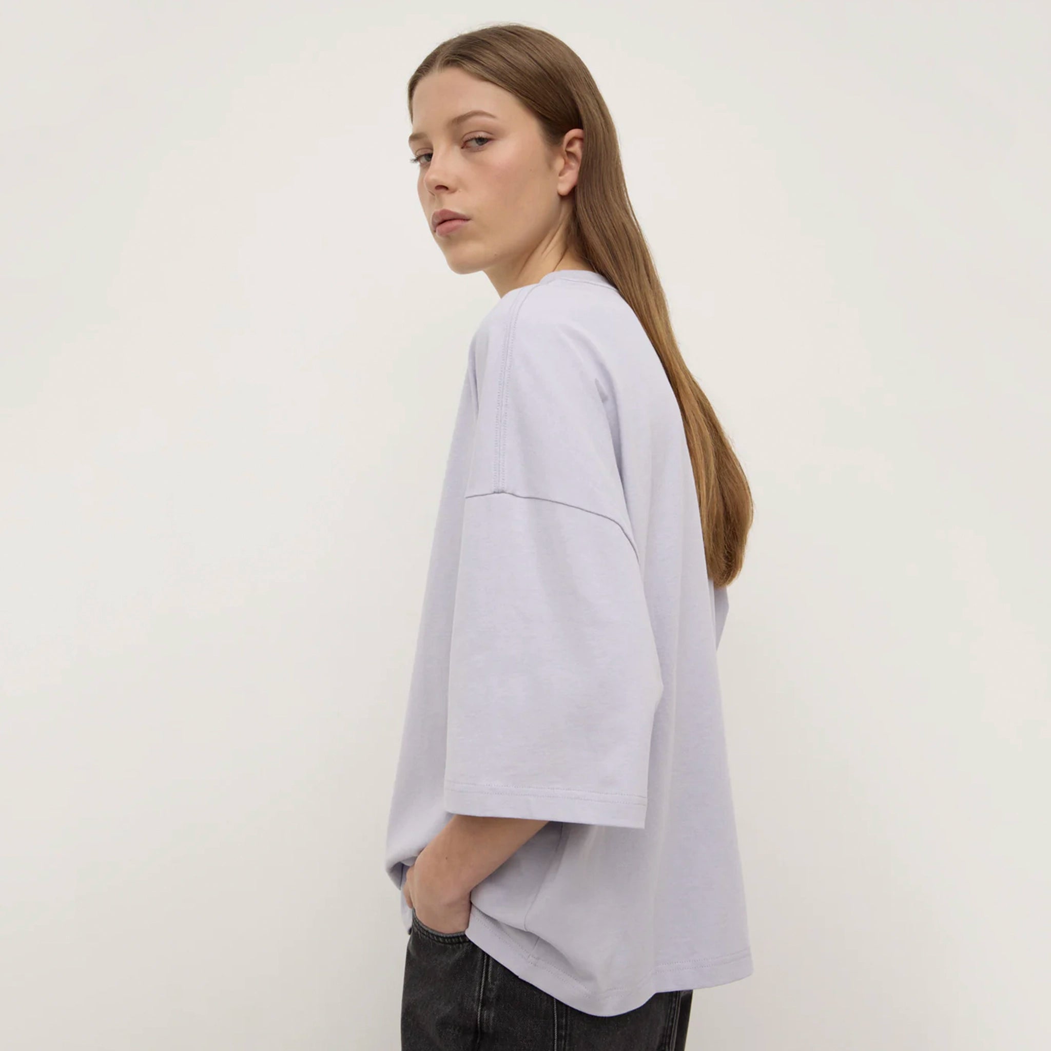 Person wearing a lilac top and dark pants against a white background