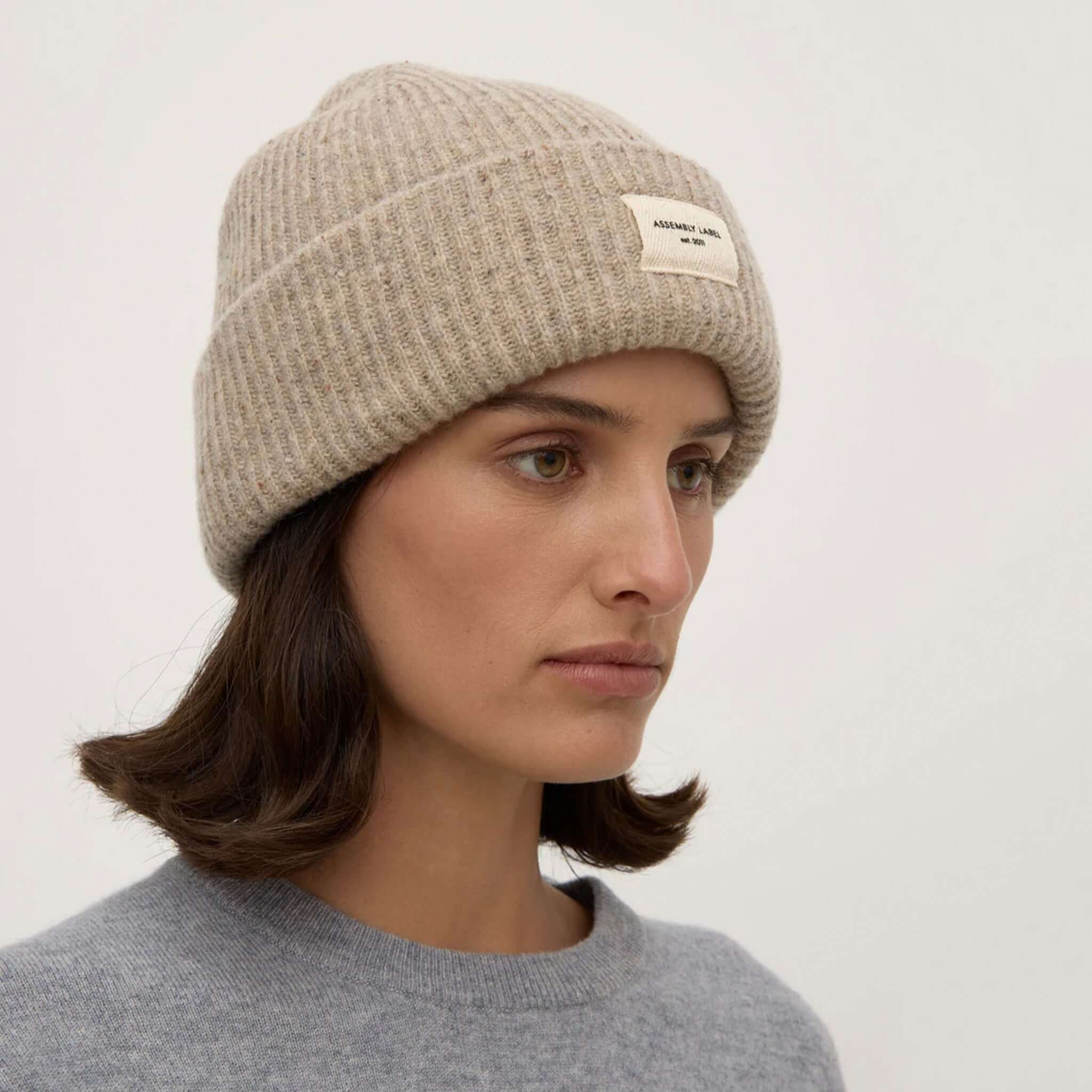 Assembly Label Merino Wool Rib Beanie - Stone Marle worn by model, showcasing the classic rib design and herringbone patch.