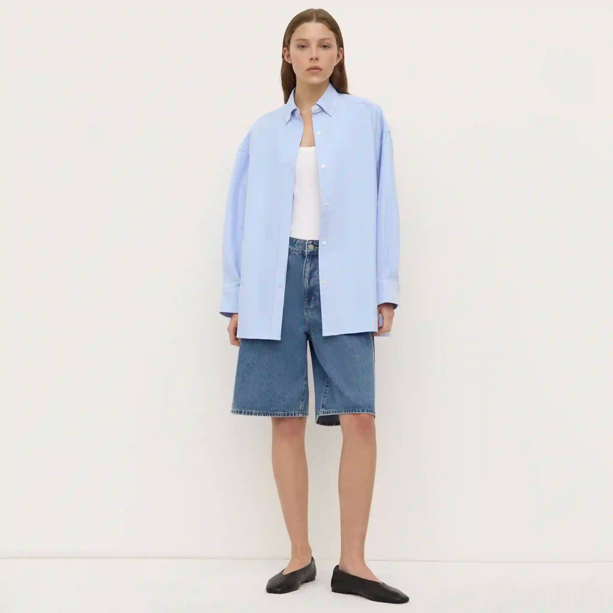 Person wearing a light blue shirt and denim shorts on a white background