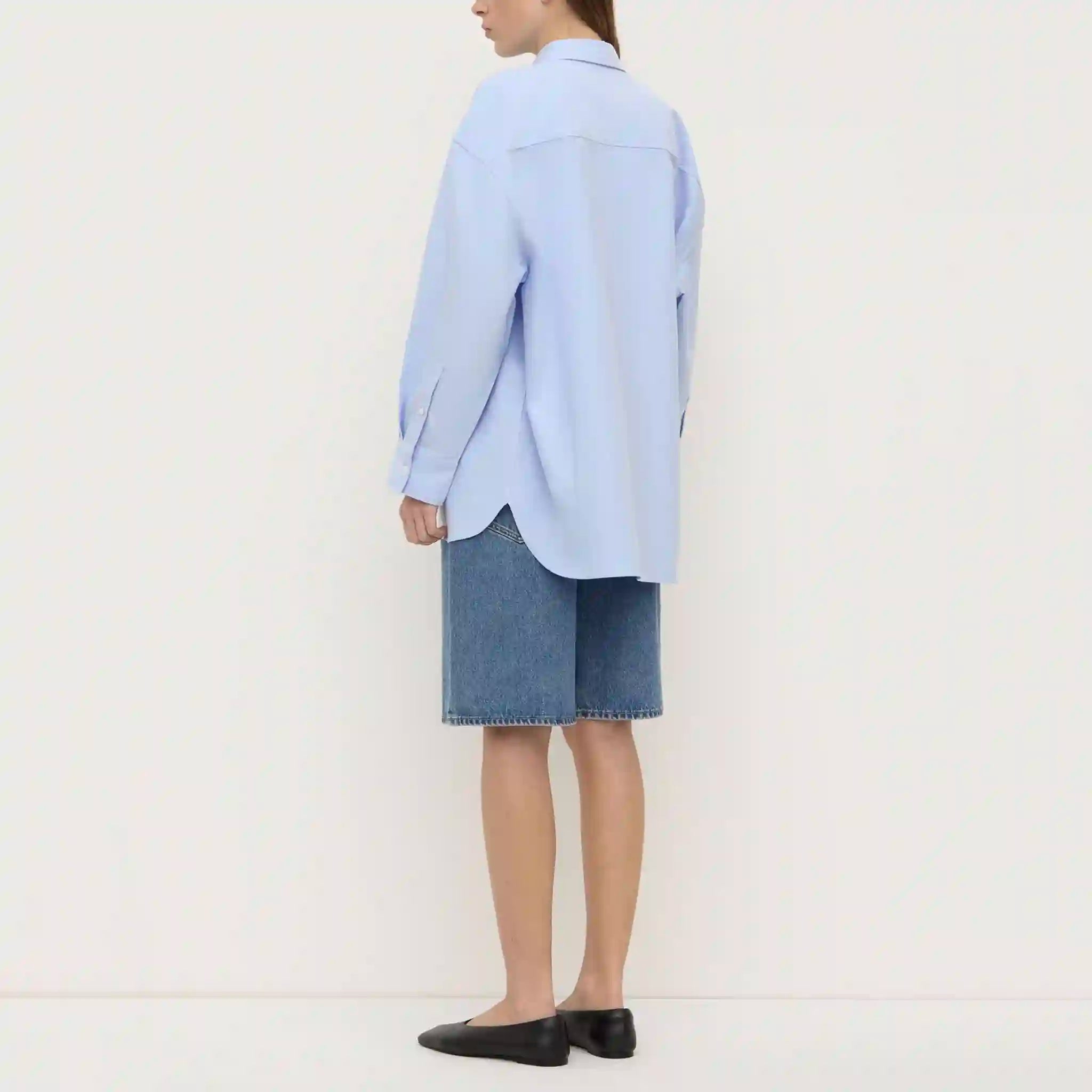 Person wearing a light blue shirt and denim skirt on a white background