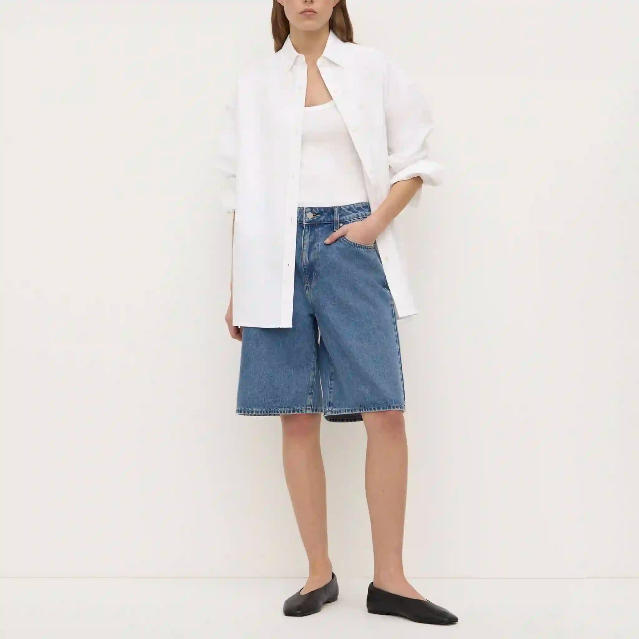 Person wearing a white blazer, white top, blue denim shorts, and black flats on a white background