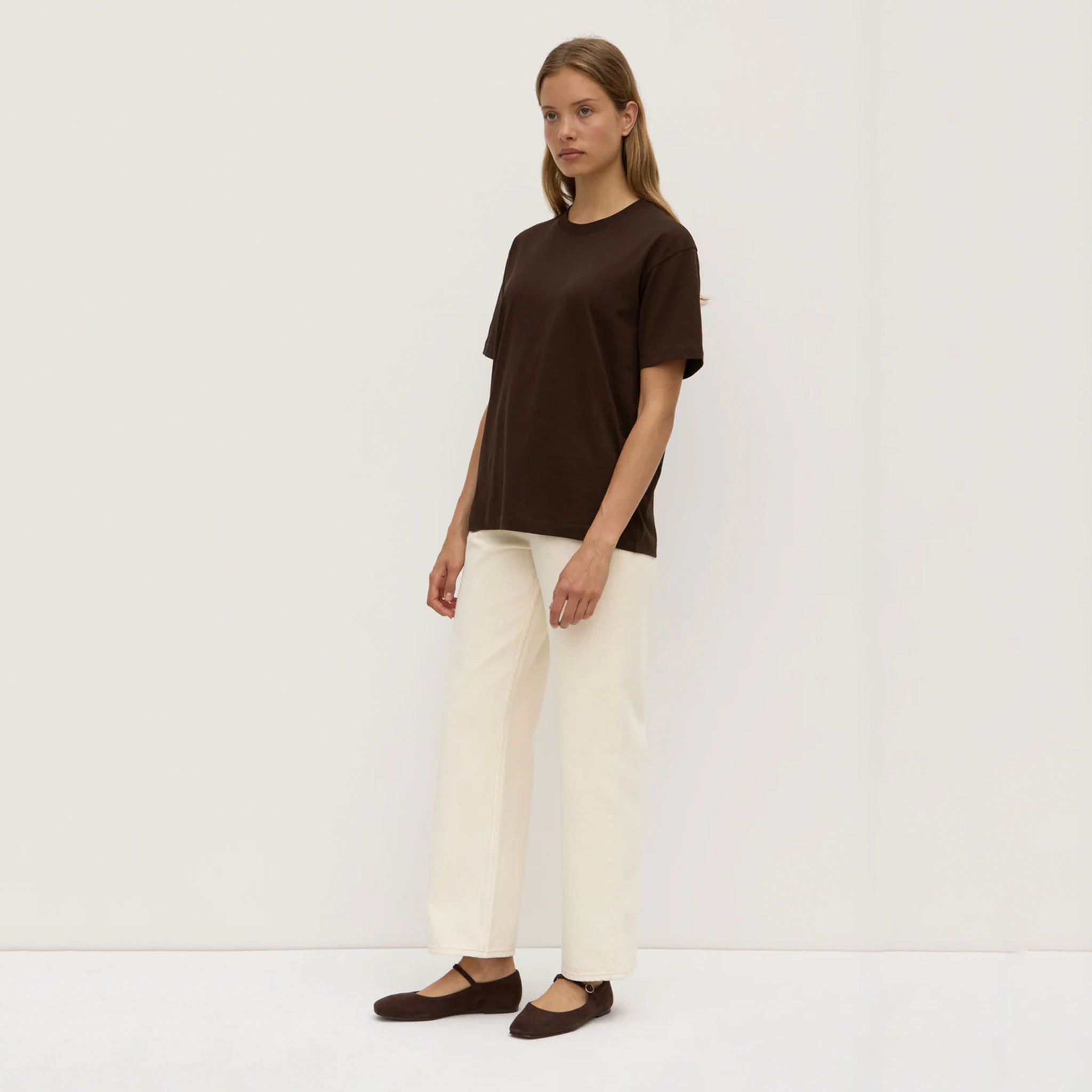 Woman wearing a brown top and white pants on a plain background