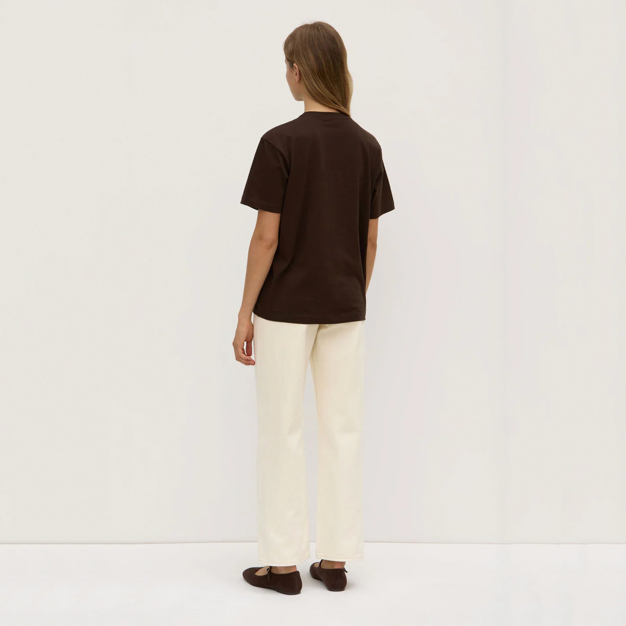 Person wearing a brown t-shirt and white pants on a plain background