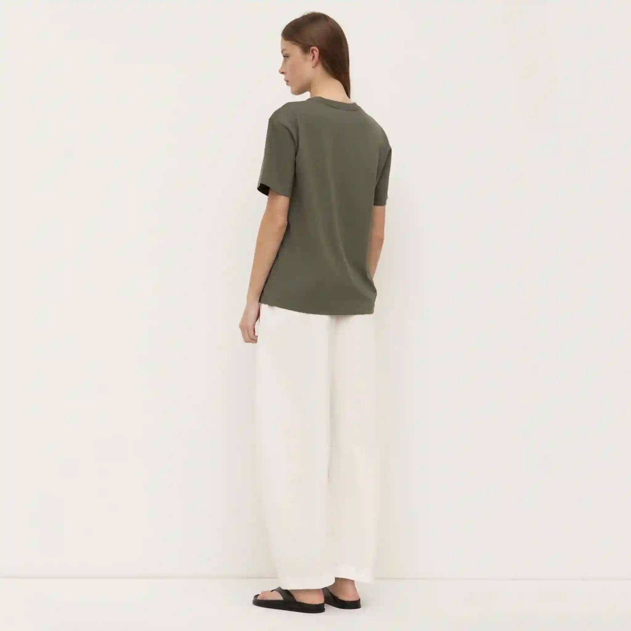 Person wearing a green t-shirt and white pants on a plain background