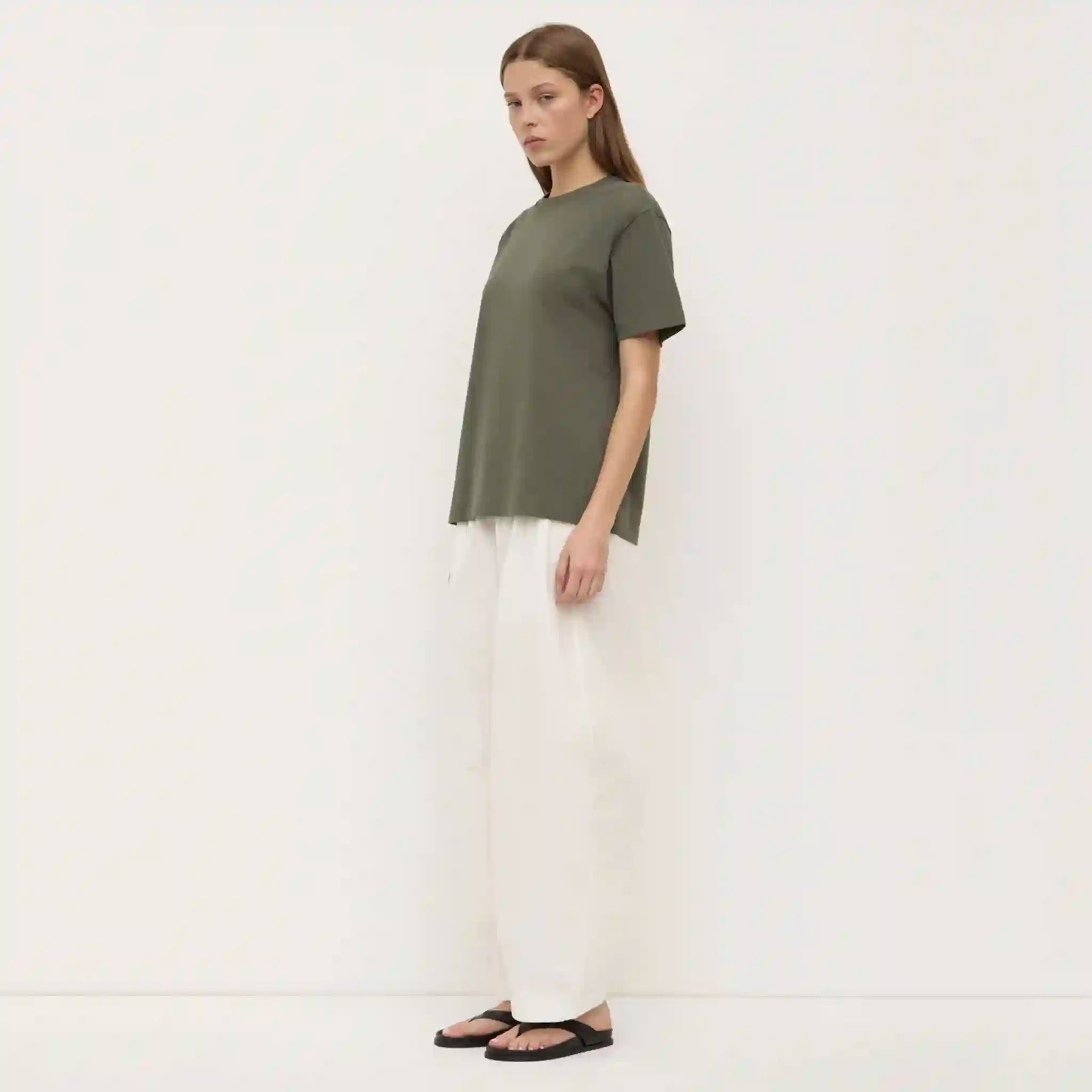 Woman wearing a green top and white pants on a white background