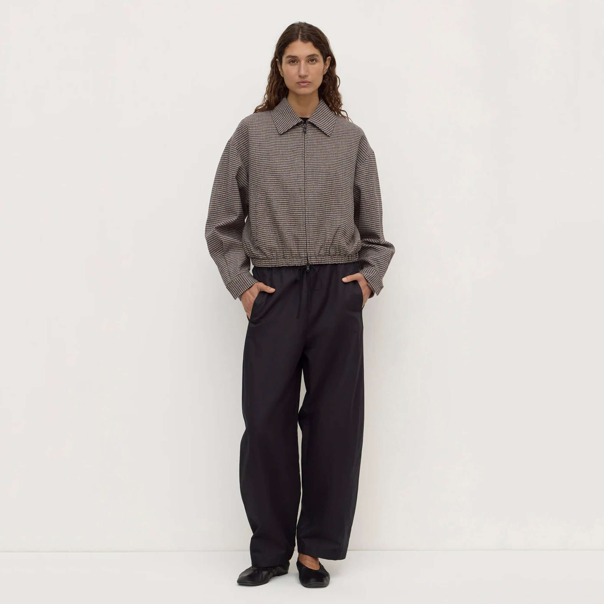 Model wearing Assembly Label Solana brown black check wool jacket with relaxed fit and gathered elastic hem.