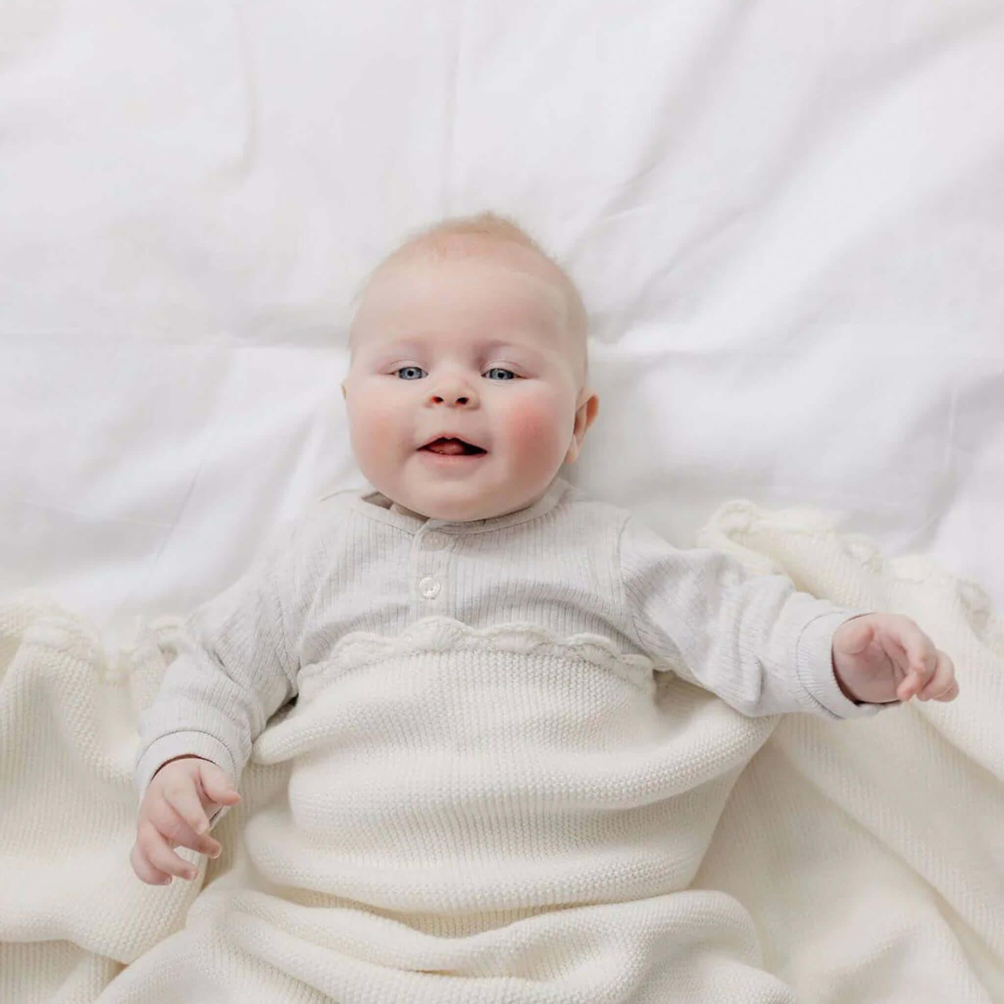 Baby Cotton Fifi Blanket - Ivory wrapped around a smiling baby on a soft white blanket.