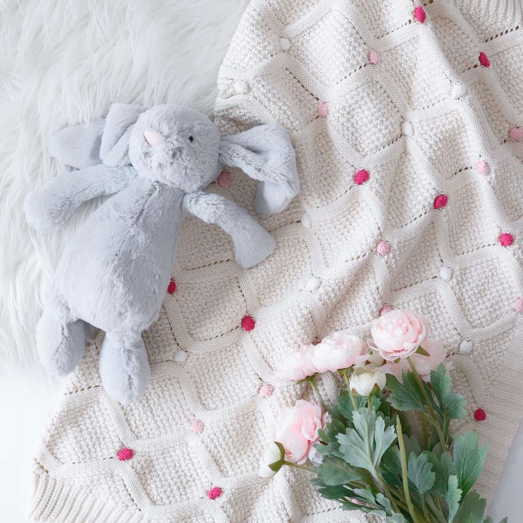 Baby Cotton Lucy Blanket - Ivory & Pink with grey bunny plush toy and pink flowers on a soft background.