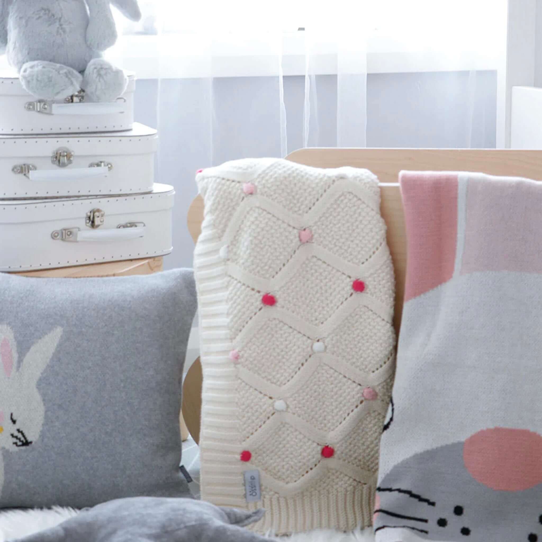 Baby Cotton Lucy Blanket - Ivory & Pink on display with decorative pillows and toys in a nursery setting.