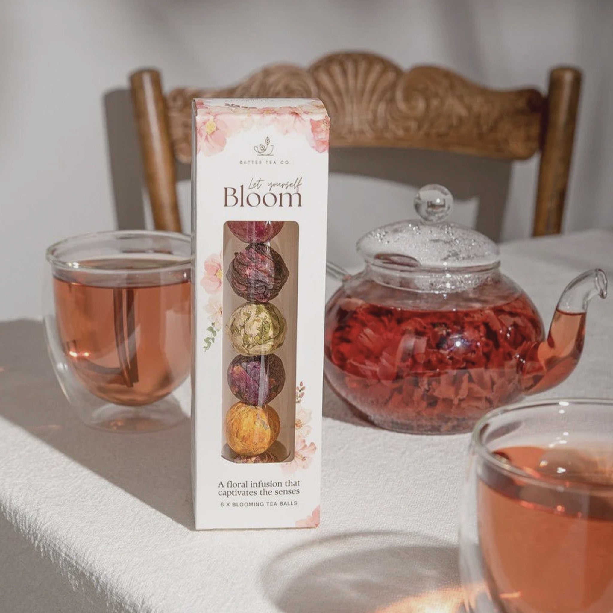 Box of 'Let Yourself Bloom' tea with a teapot and cups on a table.