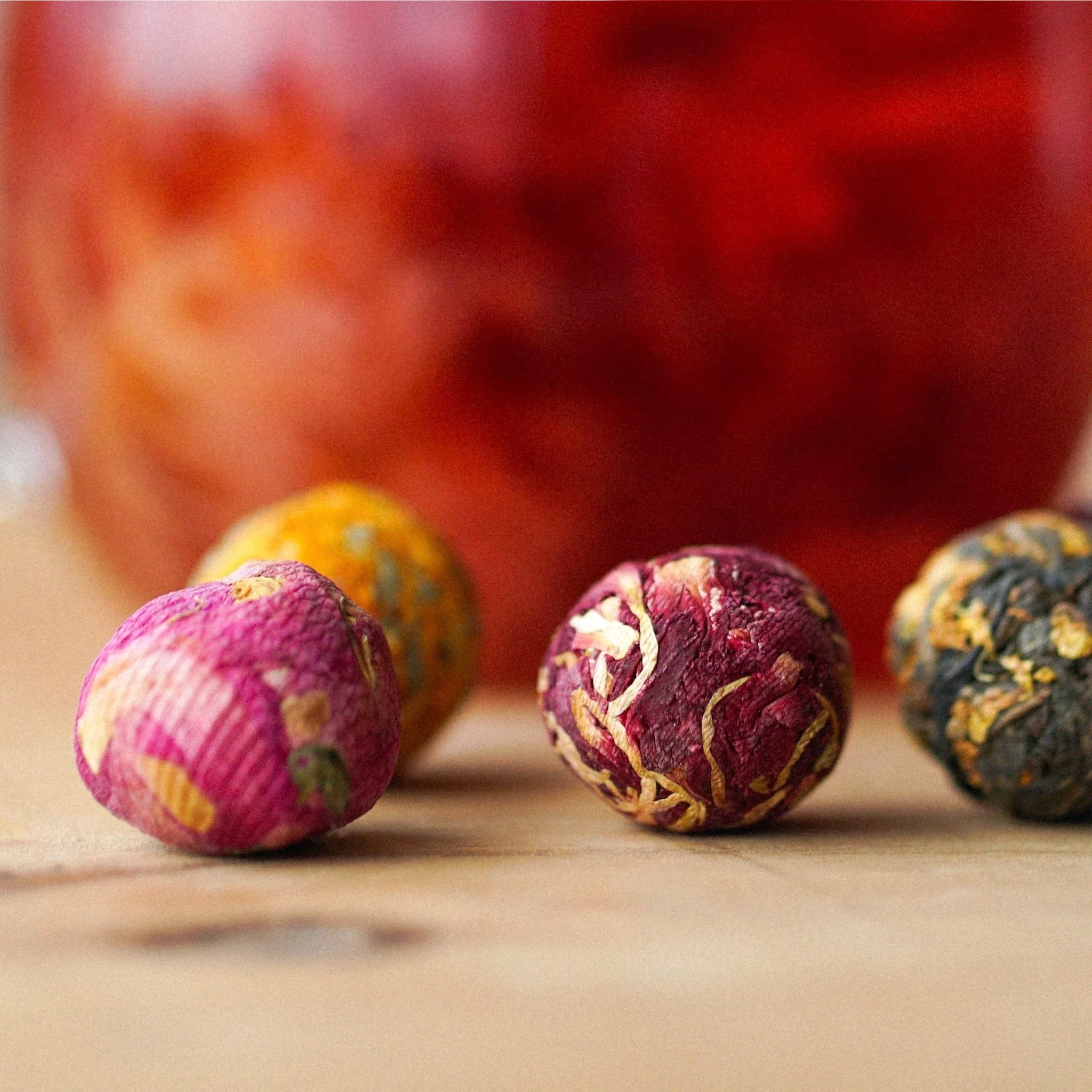 Colorful tea balls on a wooden surface with a blurred red background