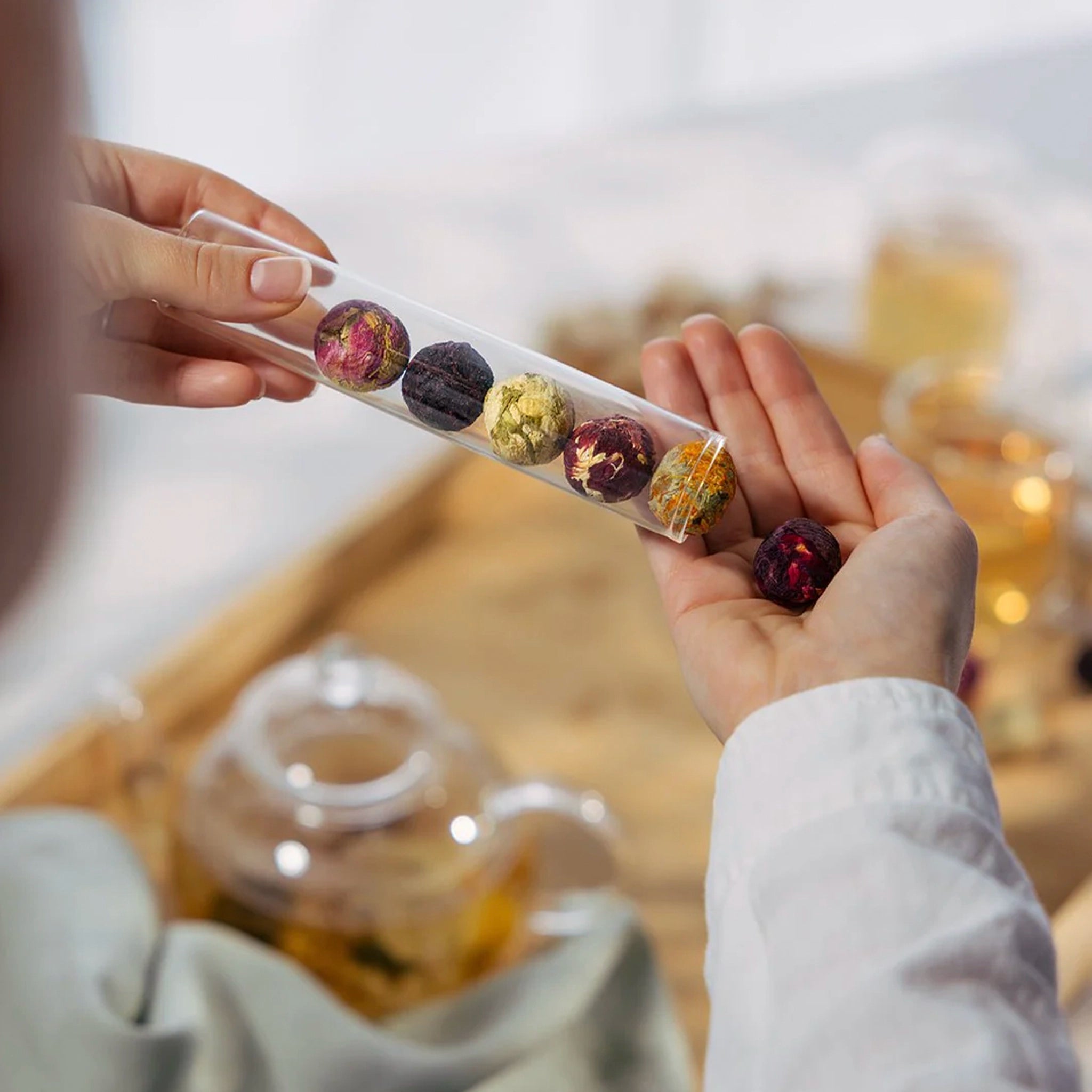 Person holding a transparent tray with various dried fruits and a blurred background of a teacup.