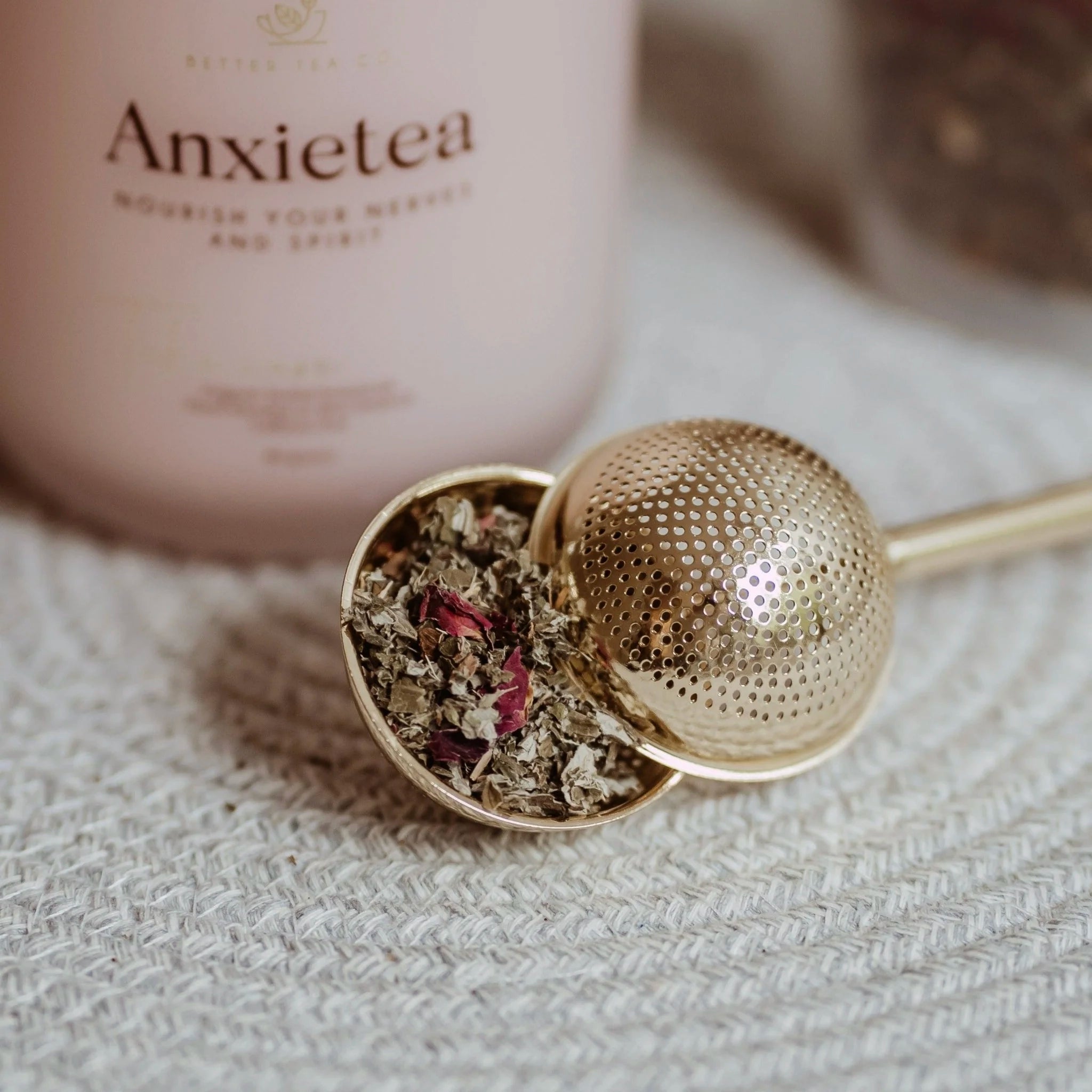 Tea infuser with dried herbs on a textured surface, Anxietea product in the background.