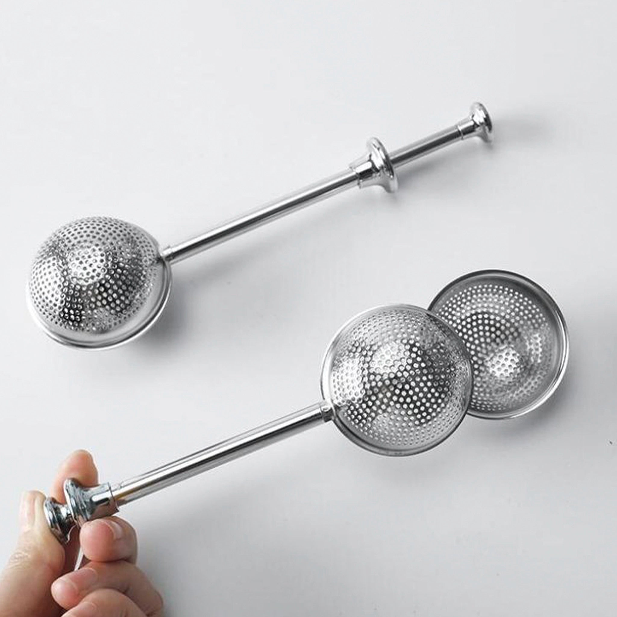 Set of three metal tea infusers on a white background