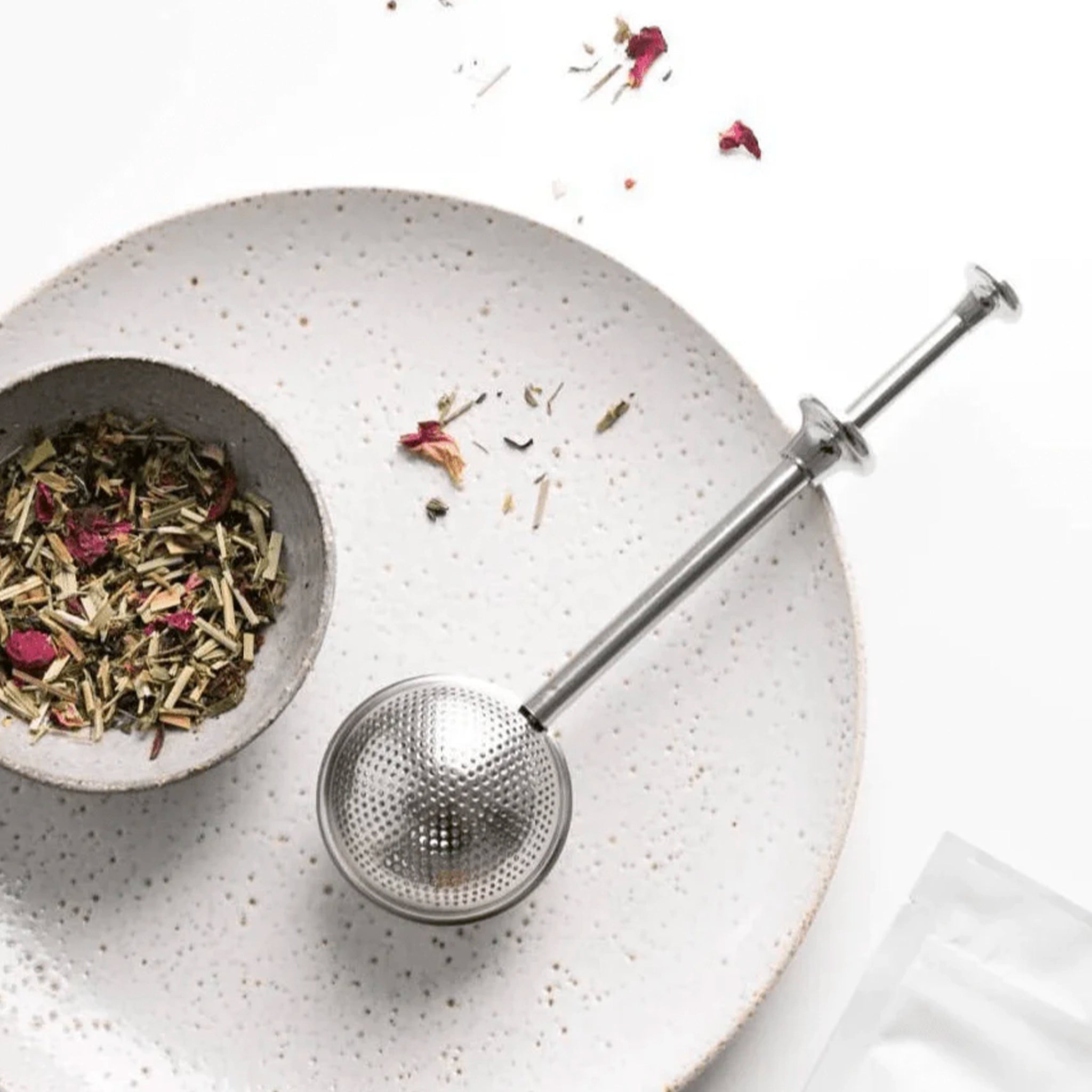 Tea strainer and bowl of tea leaves on a speckled surface