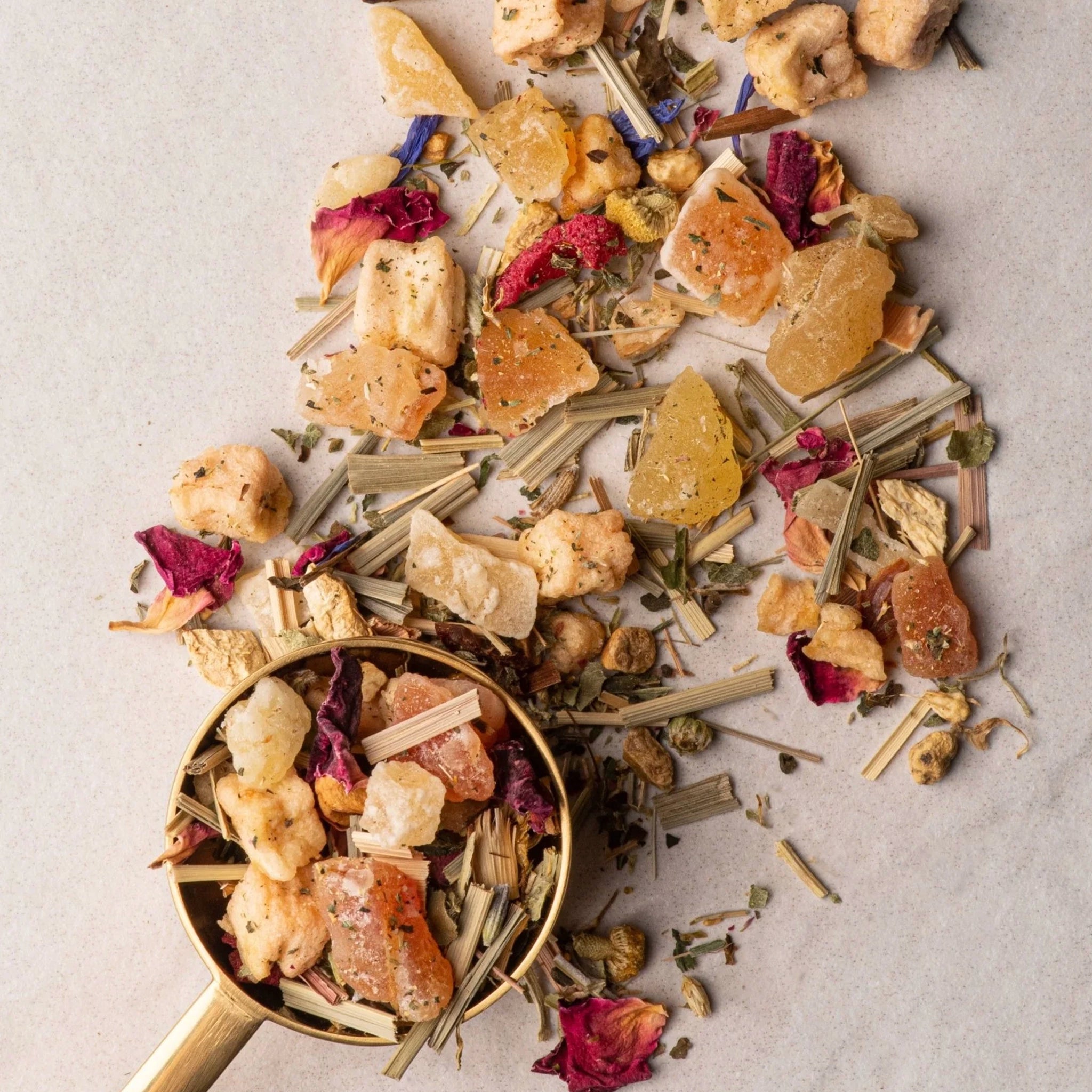 Assorted dried herbs and spices in a gold measuring spoon on a light background