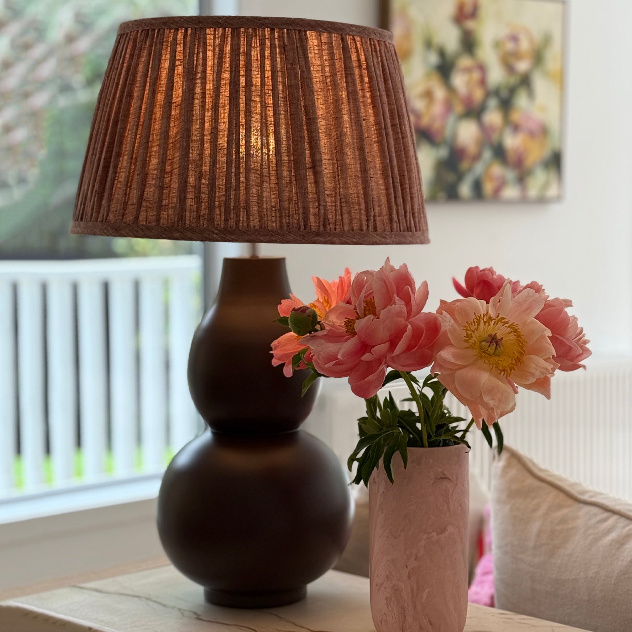 Decorative lamp with a brown shade and pink flowers in a vase on a table.
