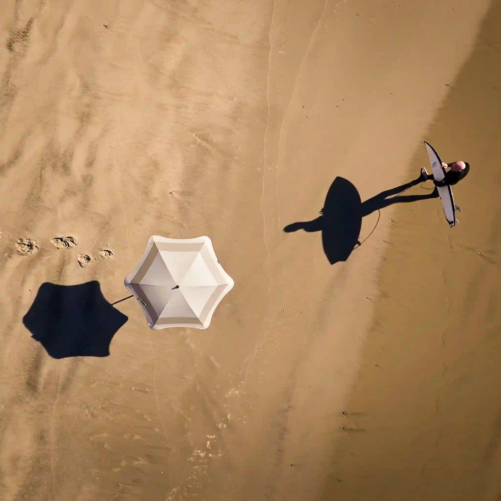 Two people with umbrellas walking on a sandy surface