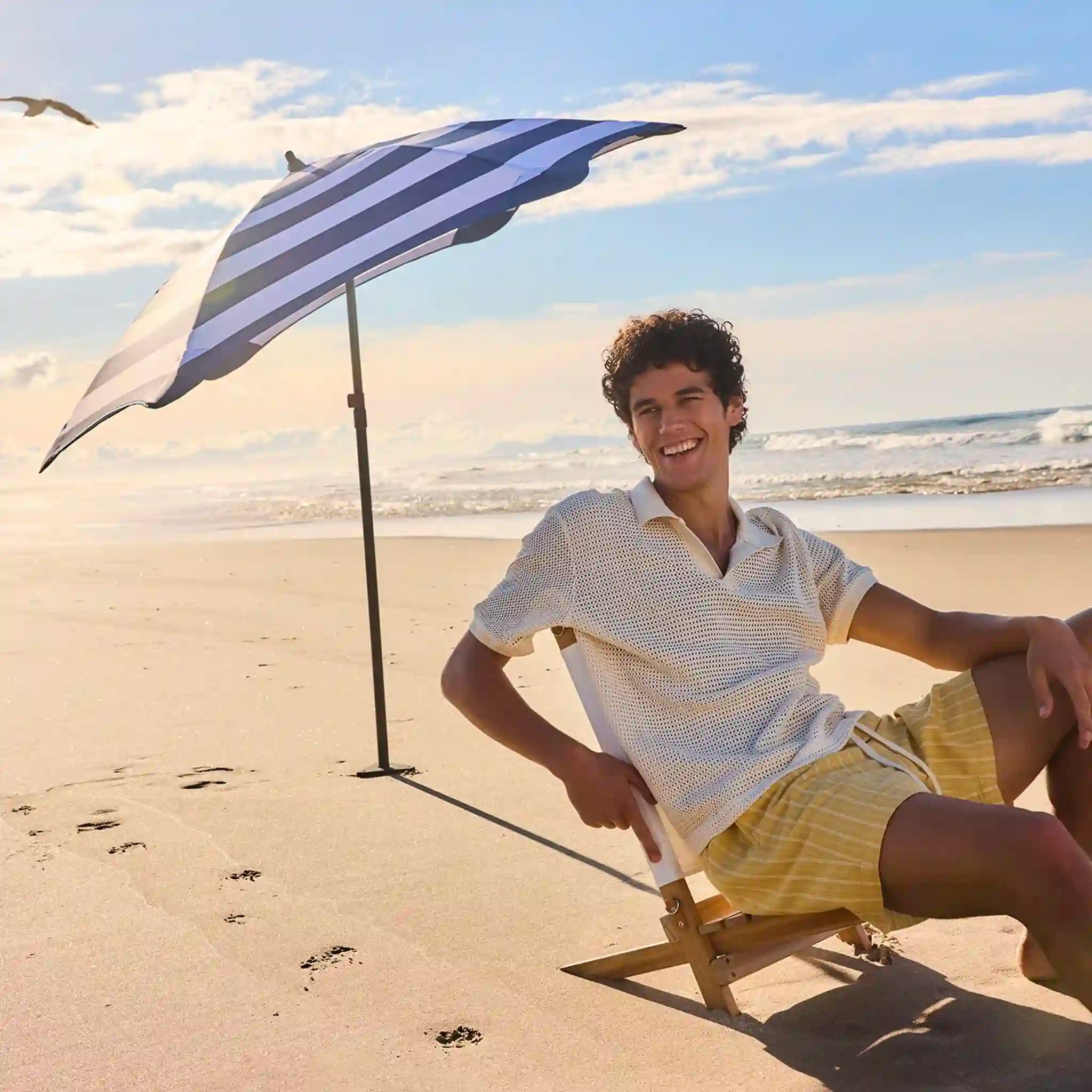 Person sitting under a striped beach umbrella on a sandy beach with ocean view