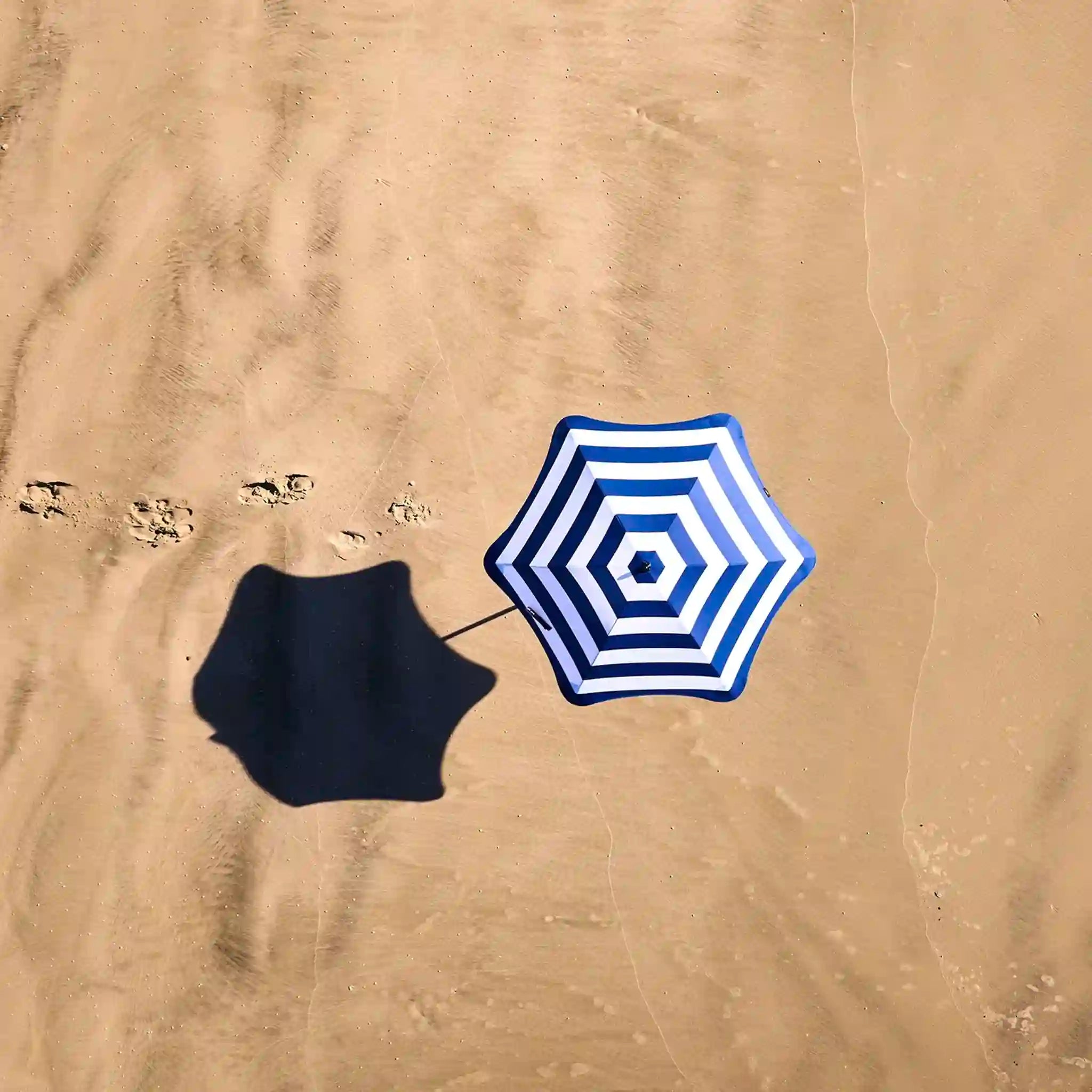 Blue and white striped beach umbrella on sandy ground