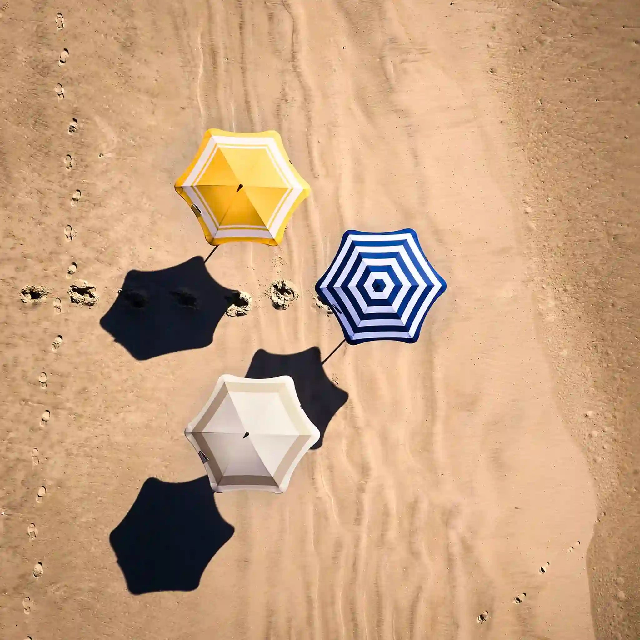 Hexagonal beach umbrellas in yellow, blue, black, and white on sandy ground.
