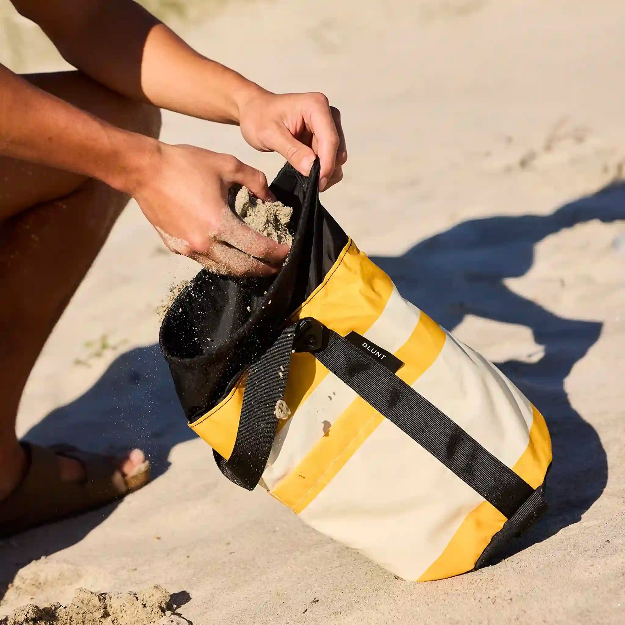 Person cleaning a yellow and black bag on a sandy surface